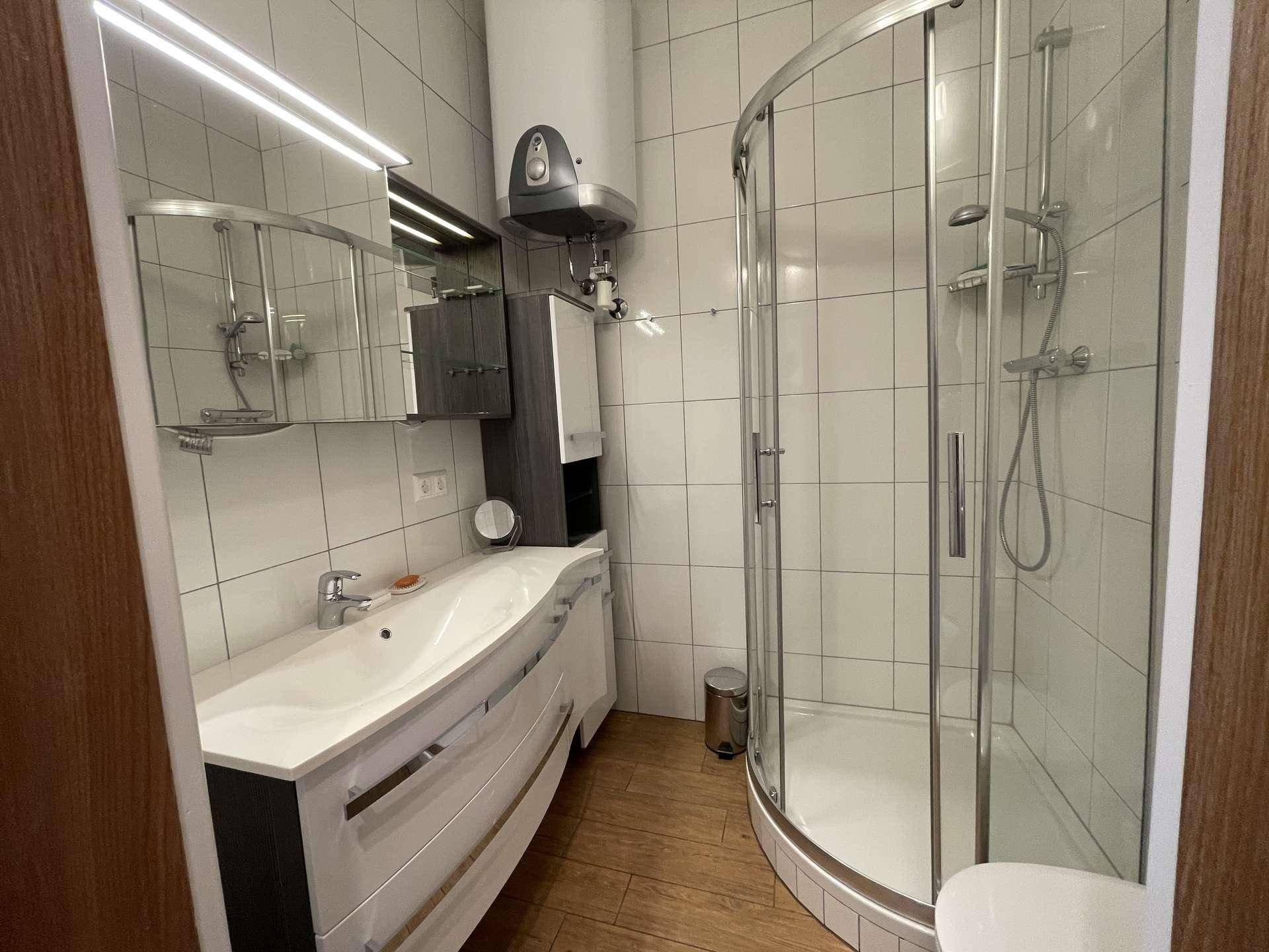 Modernes Badezimmer mit einer geräumigen Duschkabine, einem einzelnen Waschbecken und weißen Fliesen.