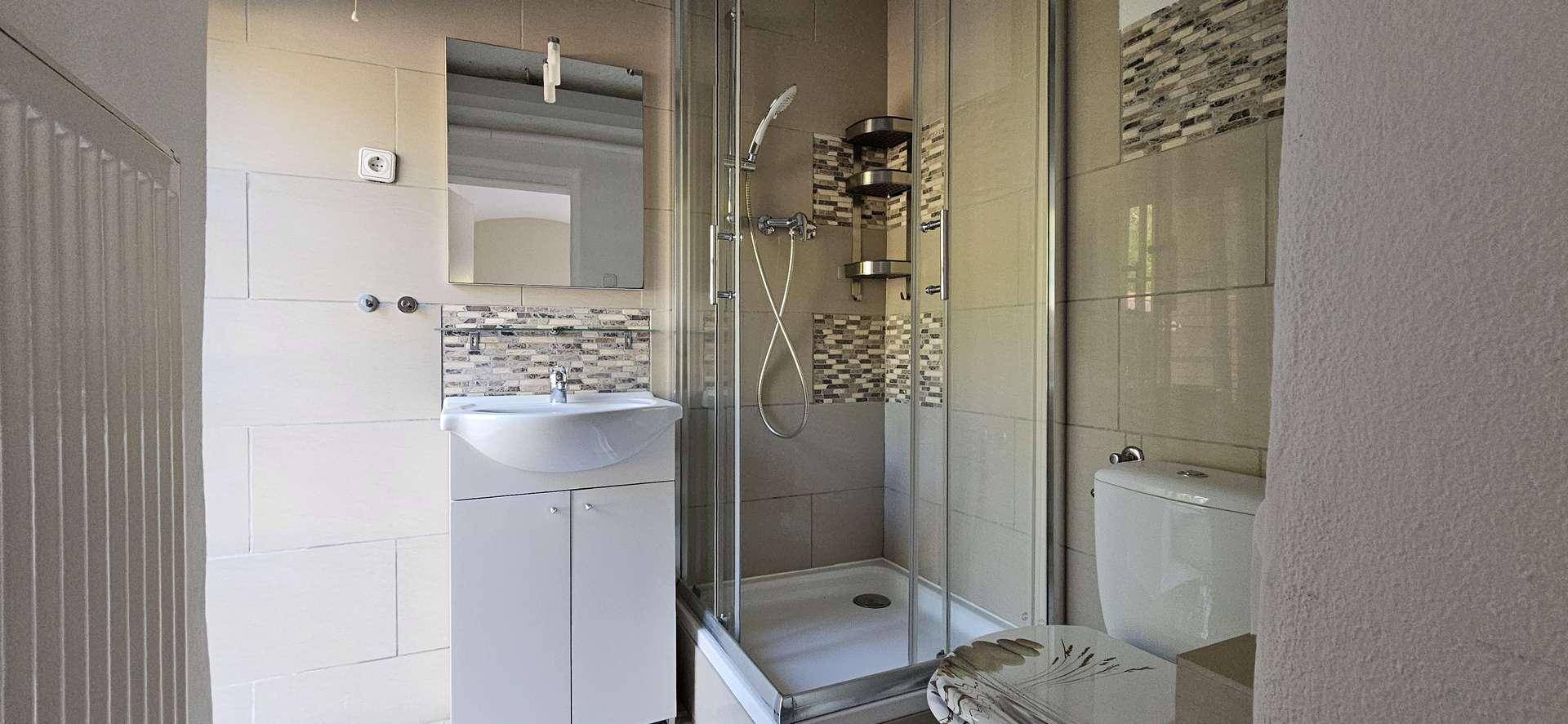 Modernes Badezimmer mit Duschkabine, Waschbeckenunterschrank und Wand-WC, ausgestattet mit hellen Fliesen.