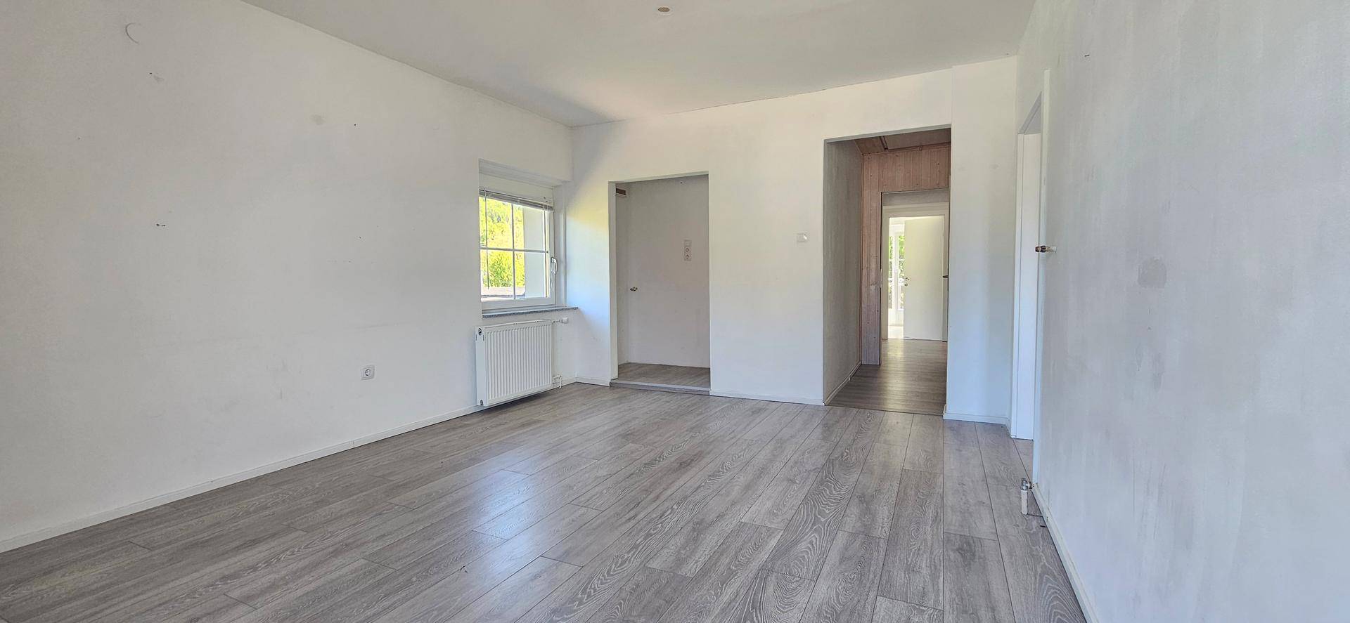 Heller Raum mit Holzboden und Fenster, der als Wohnbereich oder Flur genutzt werden könnte.