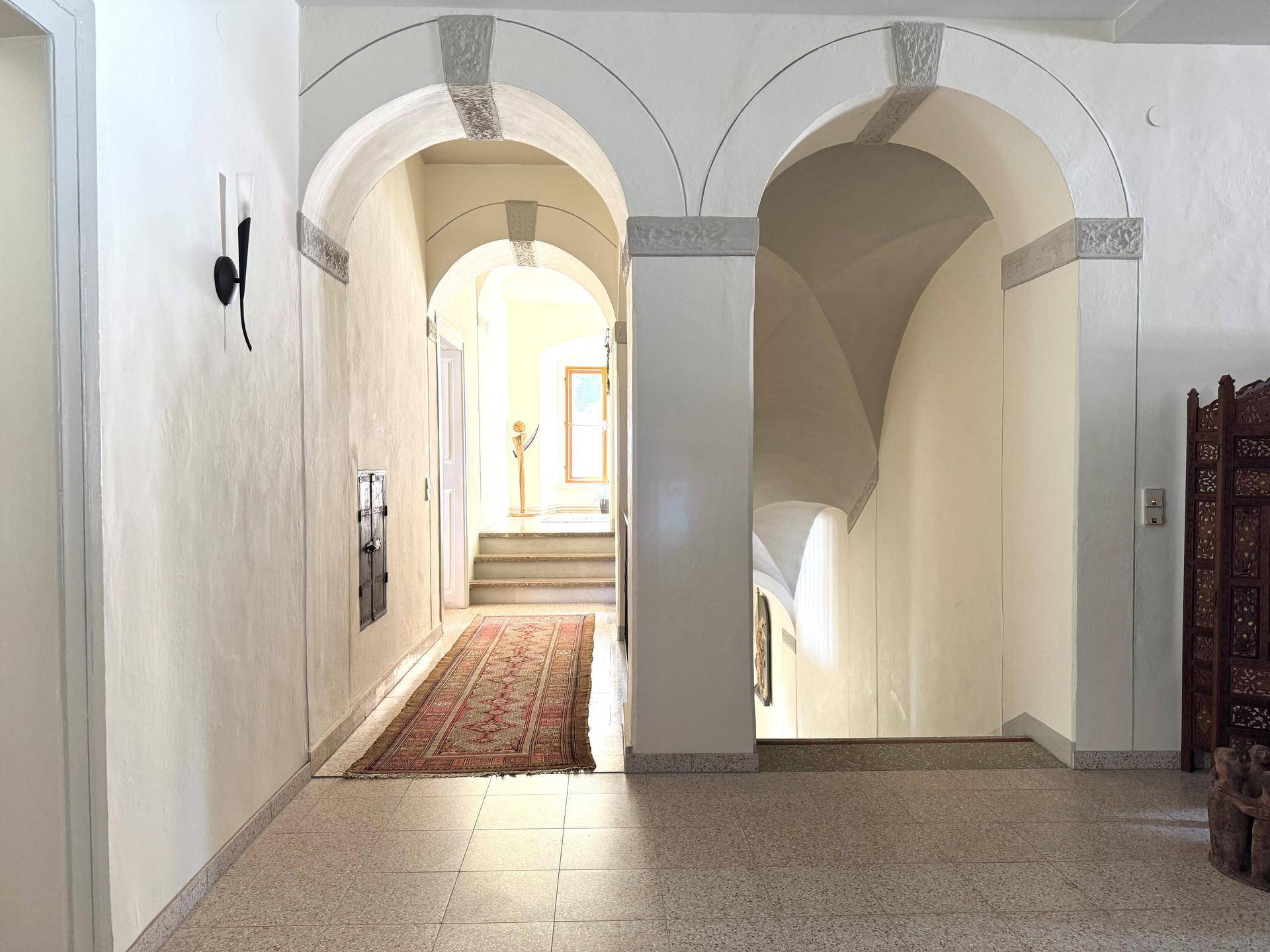 Heller Flur mit eleganten Bögen, Steinfliesenboden und Zugang zu einer Treppe.