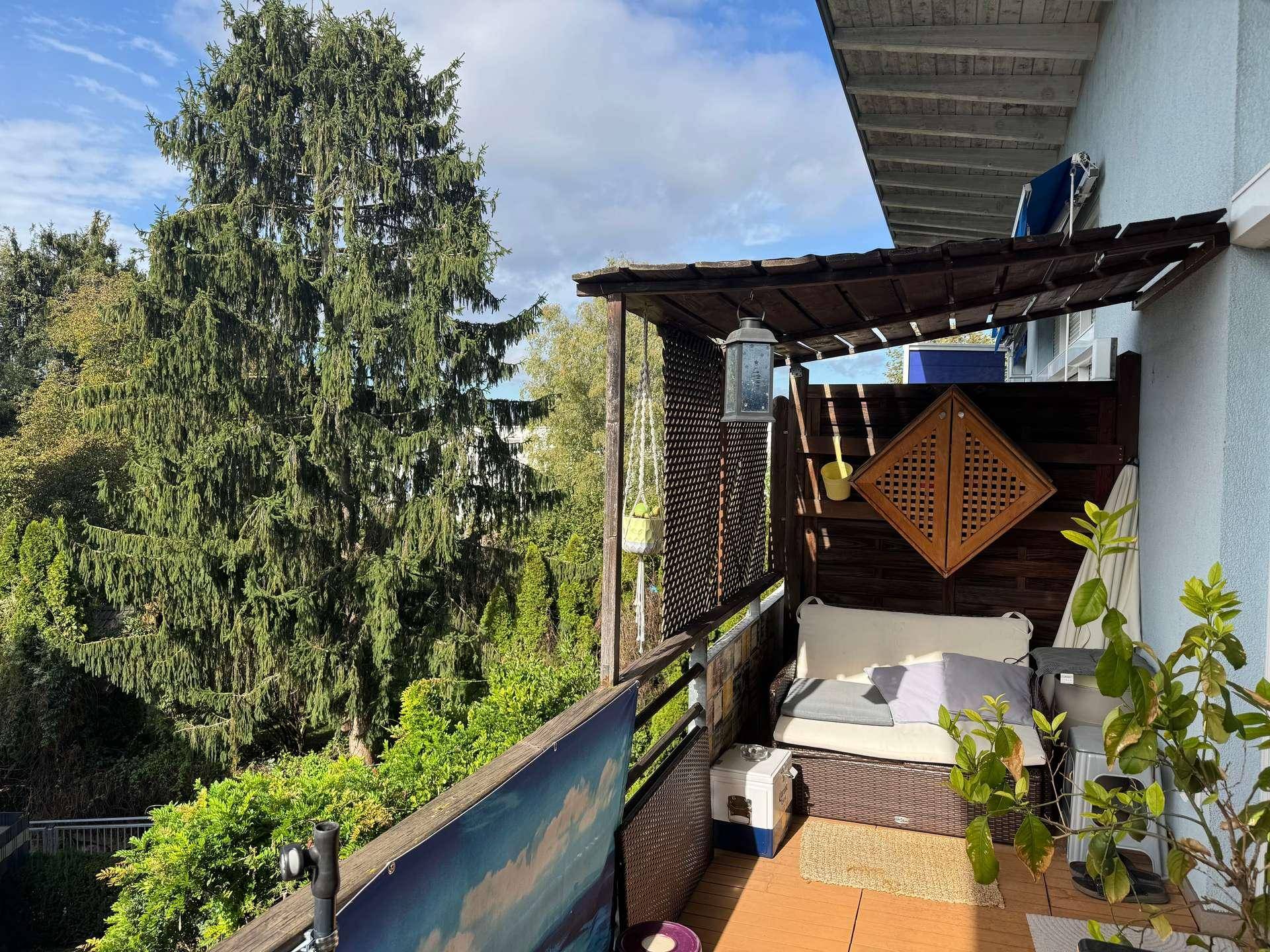 Seitlicher Balkonbereich mit gemütlicher Sitzecke, Holzelementen und Blick ins Grüne.