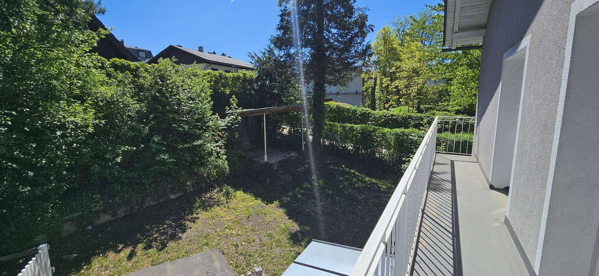 Weitläufiger Blick vom Balkon auf einen gepflegten Garten mit Hecken und einer überdachten Sitzgelegenheit.