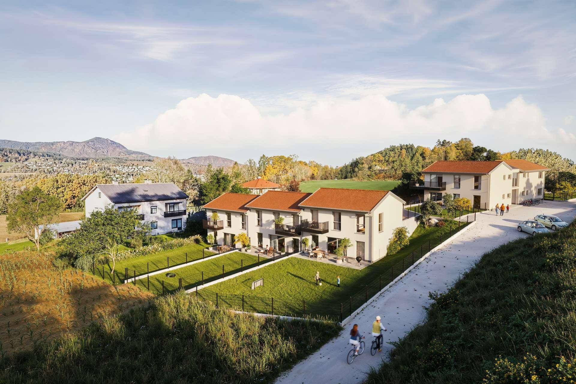 Luftaufnahme einer modernen Wohnsiedlung mit Reihenhäusern, Gärten und Bergblick.