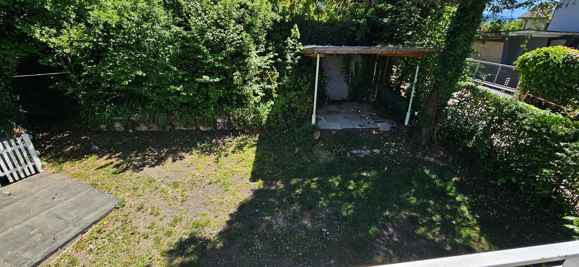 Gartenbereich mit Rasenfläche, Hecken und einer überdachten Sitzgelegenheit im Grünen.