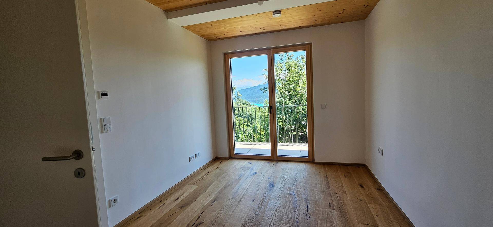 Schlafzimmer mit Holzboden, Holzdecke und Zugang zu einem Balkon mit Seeblick.