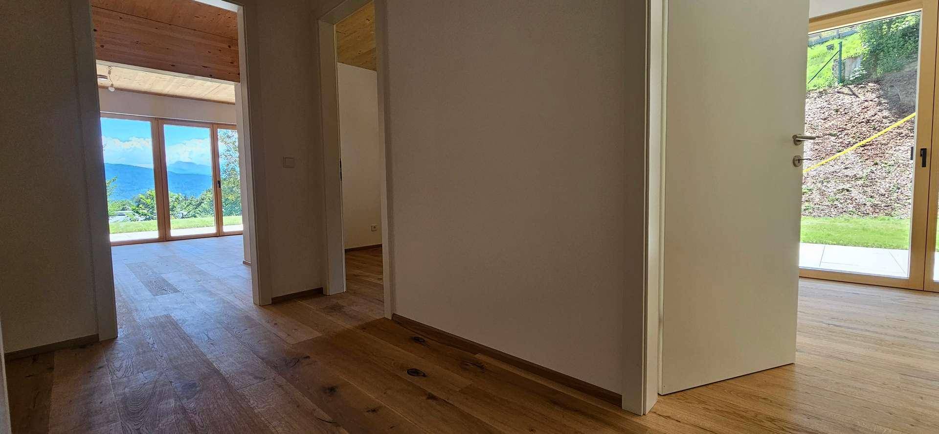 Heller Flur mit Holzboden und Holzdecke, der zu lichtdurchfluteten Räumen führt.