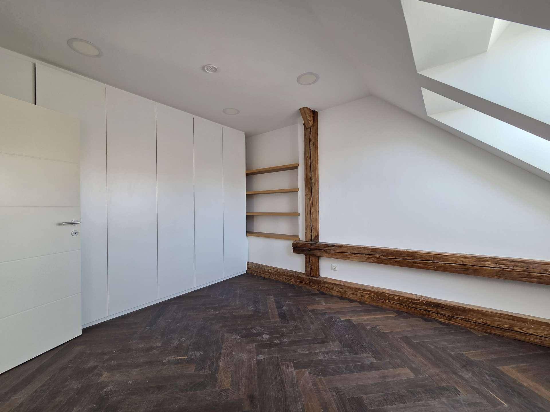 Schlafzimmer im Dachgeschoss mit weißen Einbauschränken, sichtbaren Holzbalken und Dachschräge.