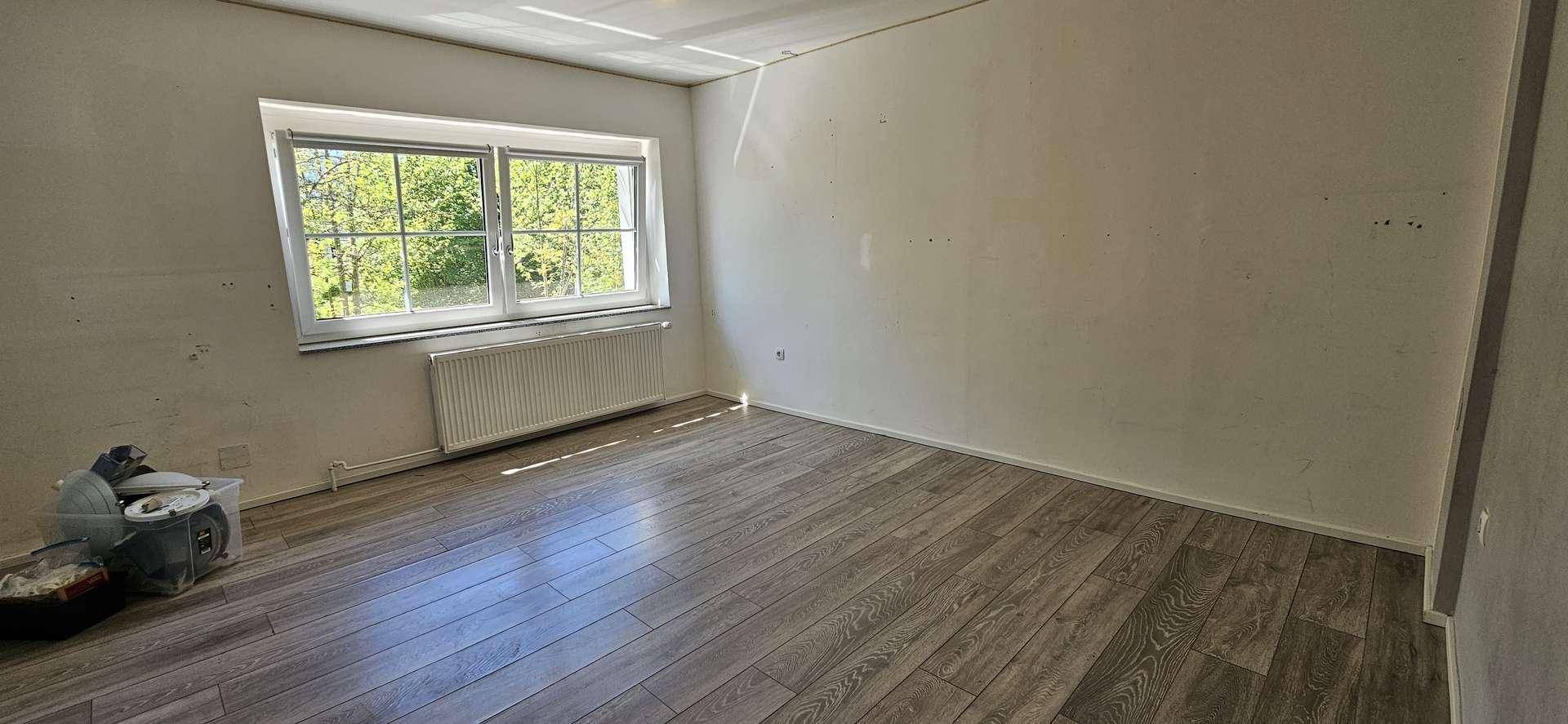 Geräumiges Schlafzimmer mit Laminatboden, weißen Wänden und einem großen Fenster für viel Tageslicht.