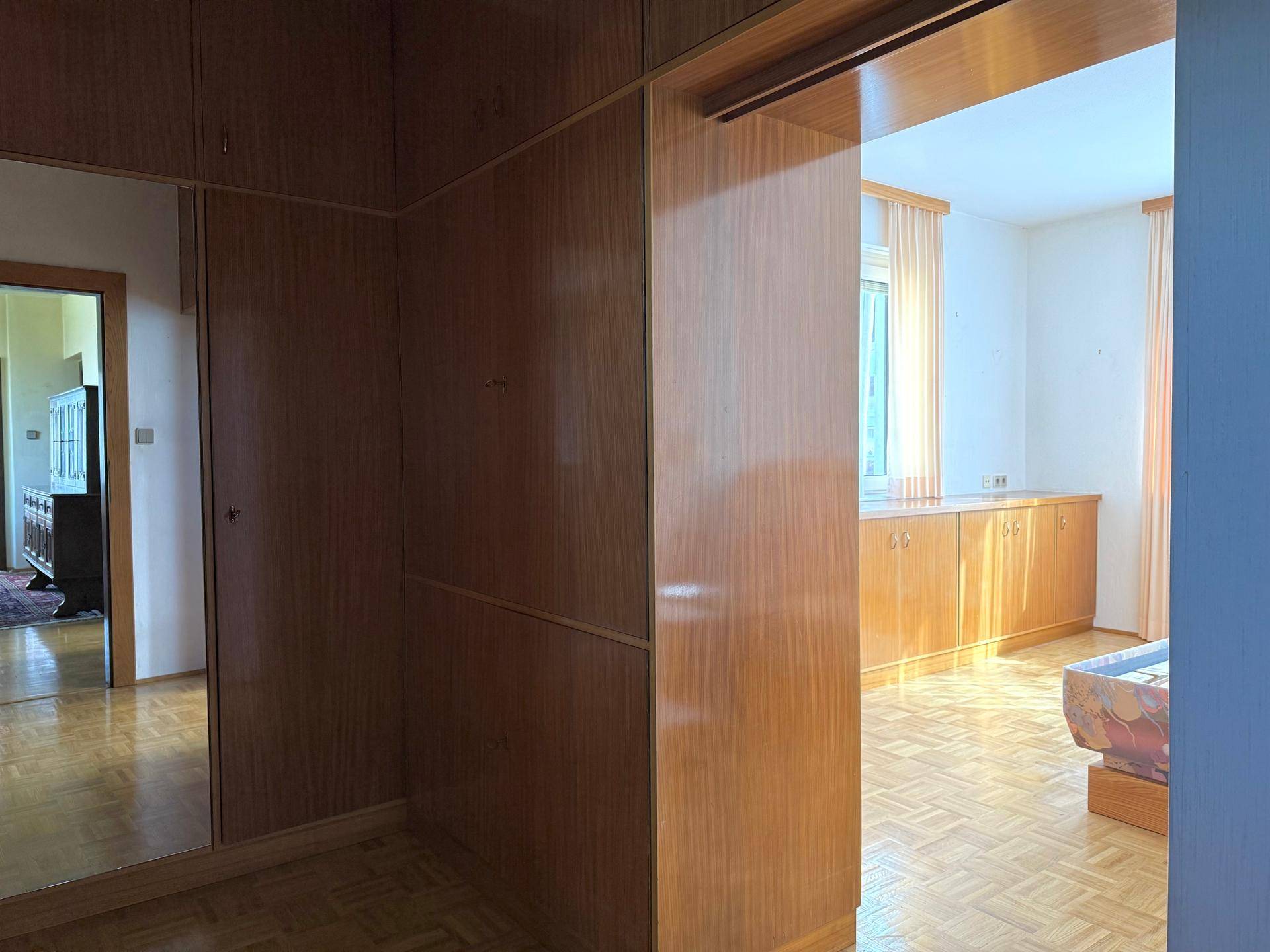 Flur mit Holzvertäfelung und Blick in ein weiteres Zimmer mit Parkettboden und Tageslicht.