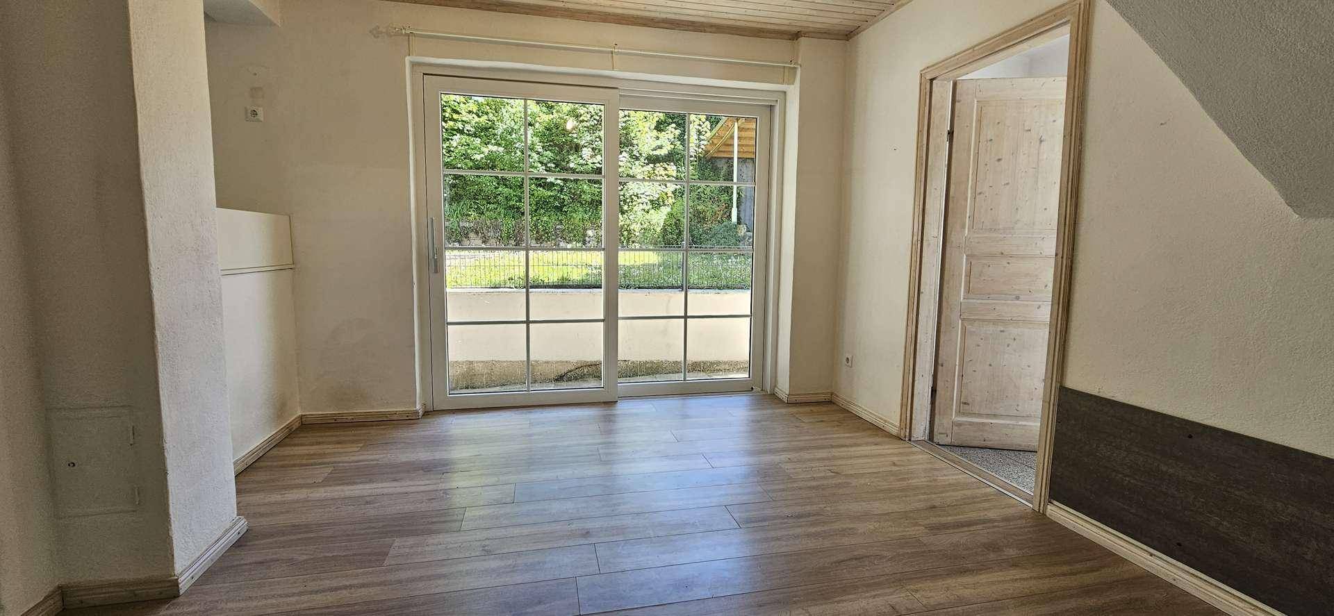 Heller Wohnraum mit Laminatboden, Holzdielen-Decke und großer Glasschiebetür zum Außenbereich.