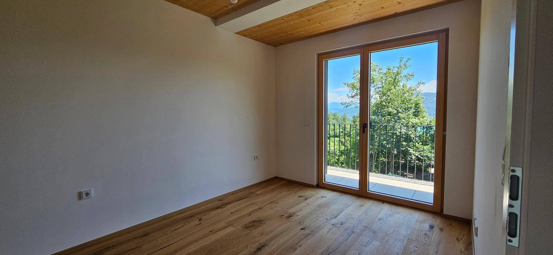 Schlafzimmer mit Holzboden und Holzdecke, großen Fenstern und Zugang zum Balkon mit Bergblick.
