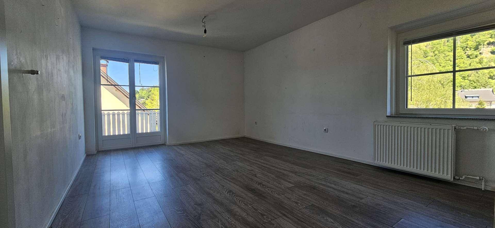 Helles Schlafzimmer mit Laminatboden, Heizkörper und Balkonzugang, bietet einen Ausblick ins Grüne.
