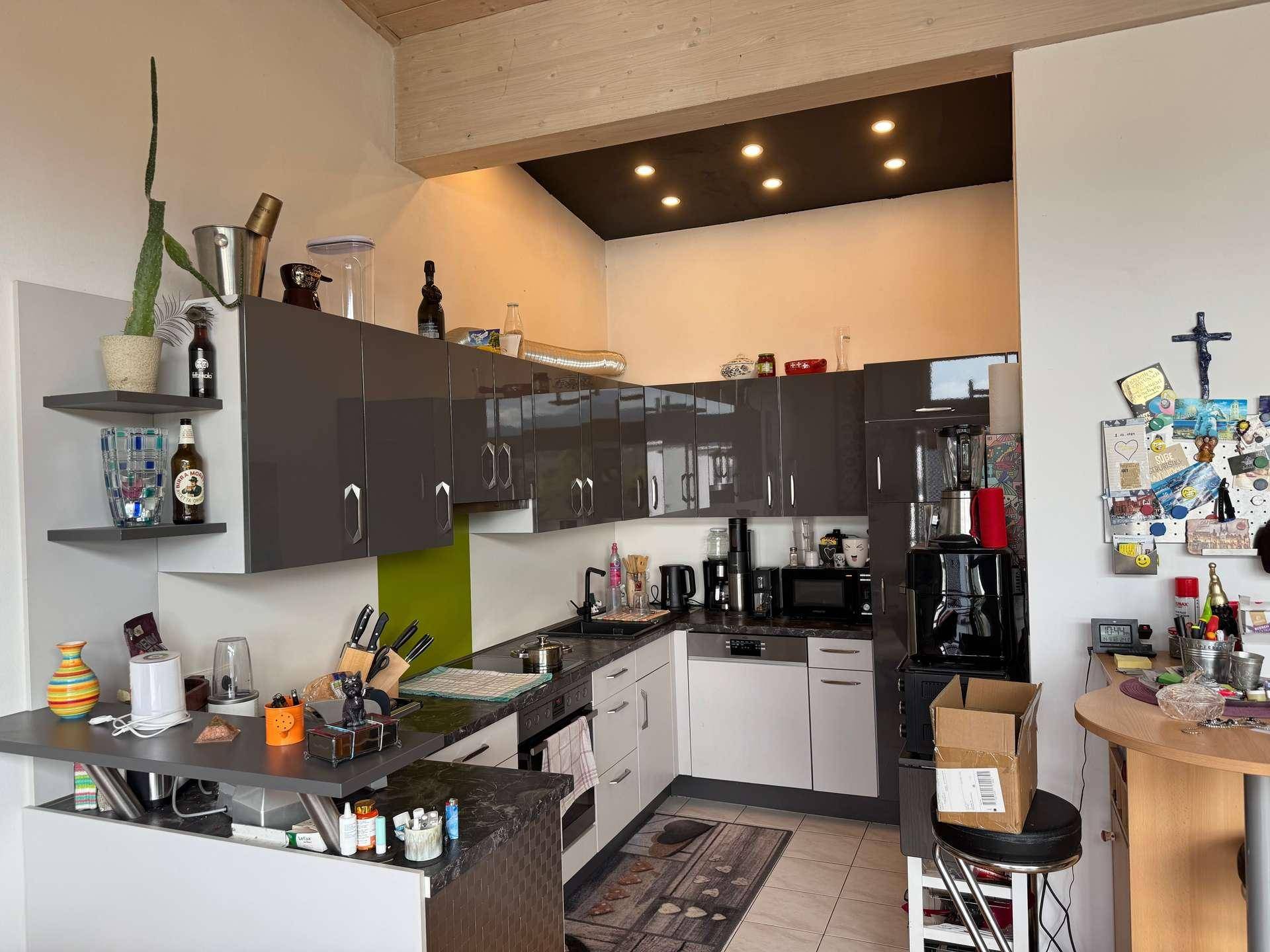 Moderne Küche mit grauen Hochglanzschränken, Fliesenboden und integrierter Frühstücksbar.