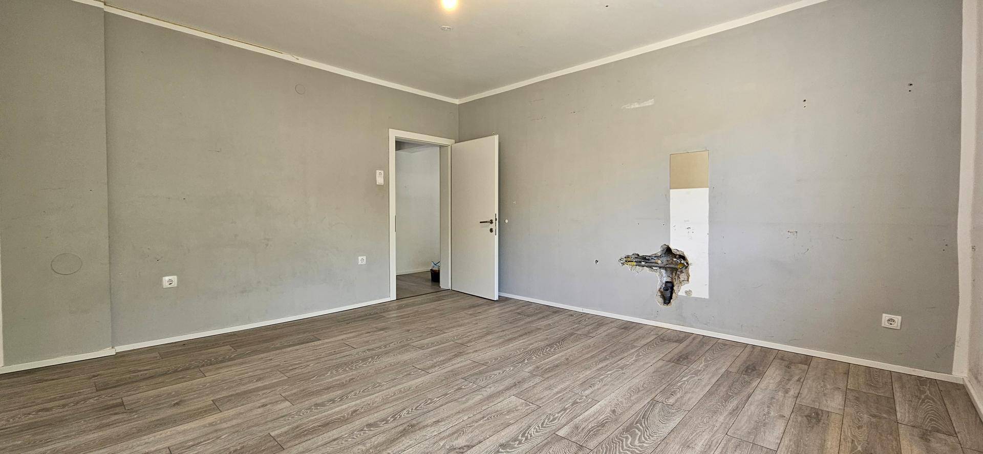Schlafzimmer mit Holzboden und grauen Wänden, das Renovierungsbedarf aufweist.