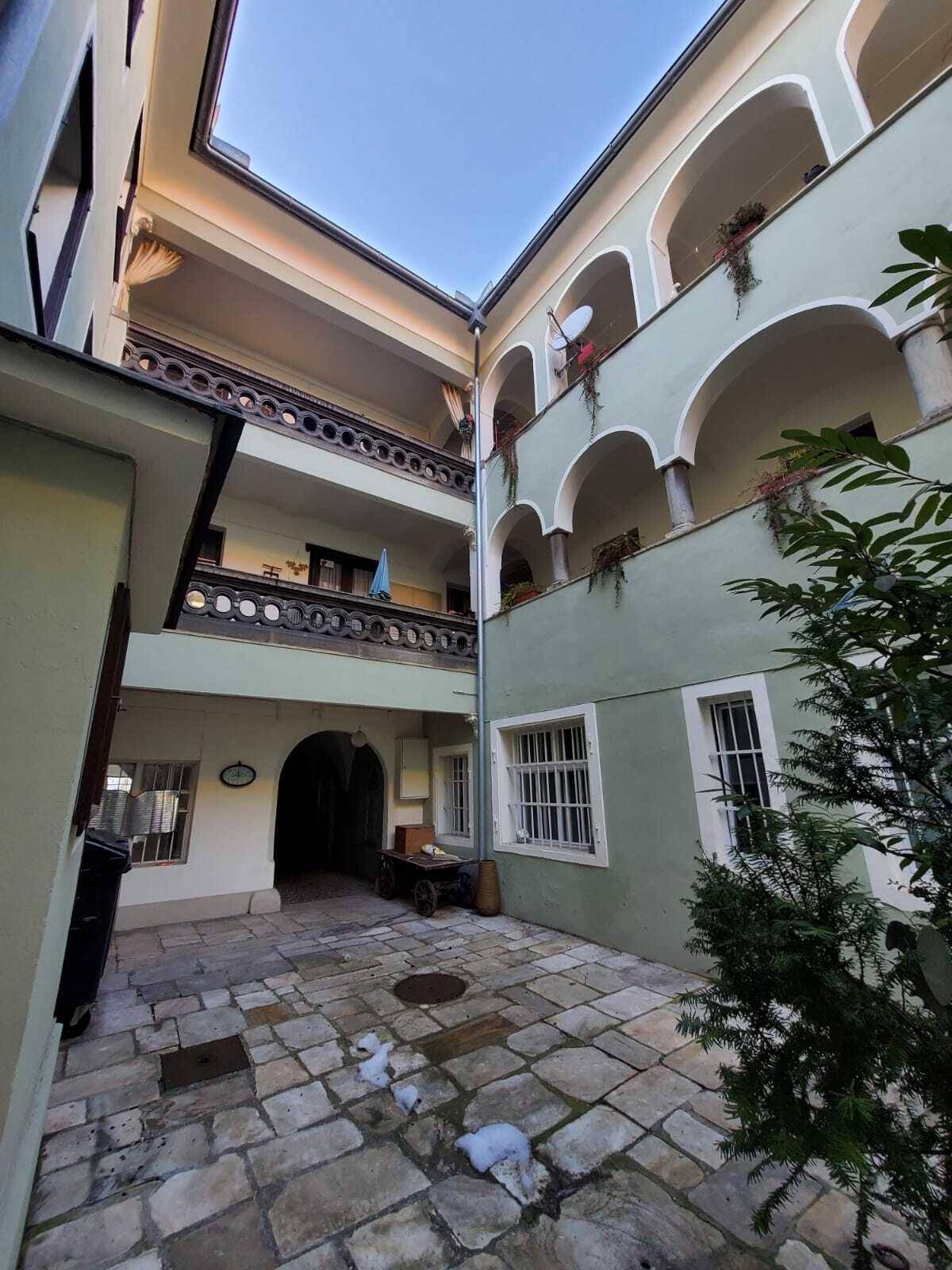 Historischer Innenhof mit Steinpflaster, Arkaden und einem traditionellen Holzbalkon.