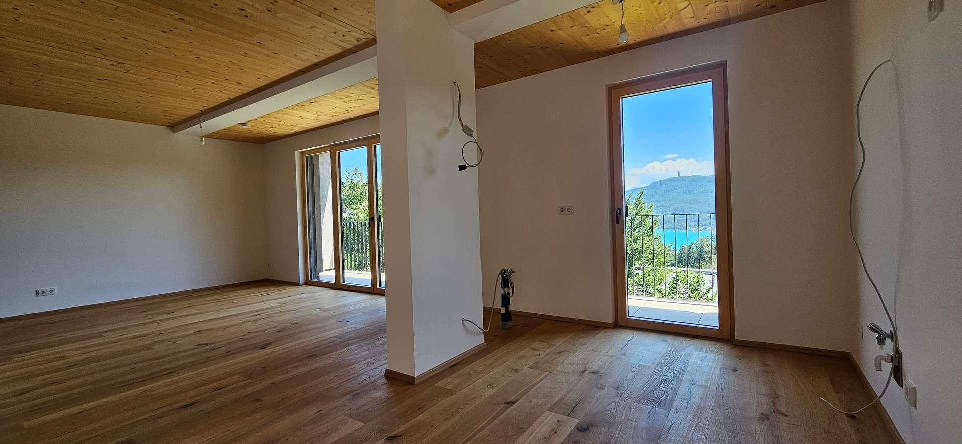 Heller, leerer Raum mit Holzboden und Holzdecke, großen Fenstern und Seeblick.