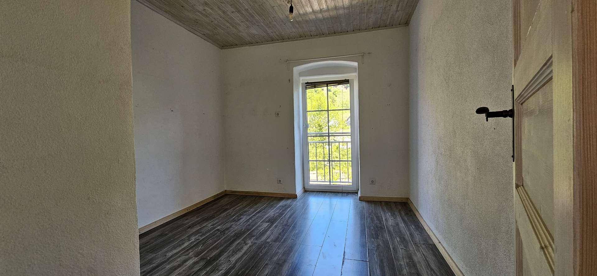 Helles Schlafzimmer mit Laminatboden, weißen Wänden und einem französischen Balkon mit Blick ins Grüne.