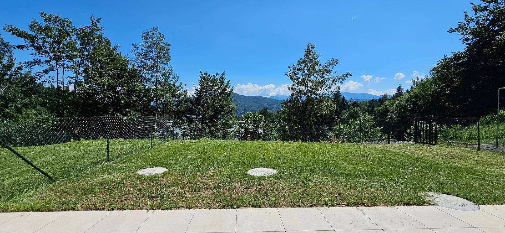 Gepflegte Rasenfläche mit Zaun und einem weiten Blick auf die umliegenden Berge und Wälder.
