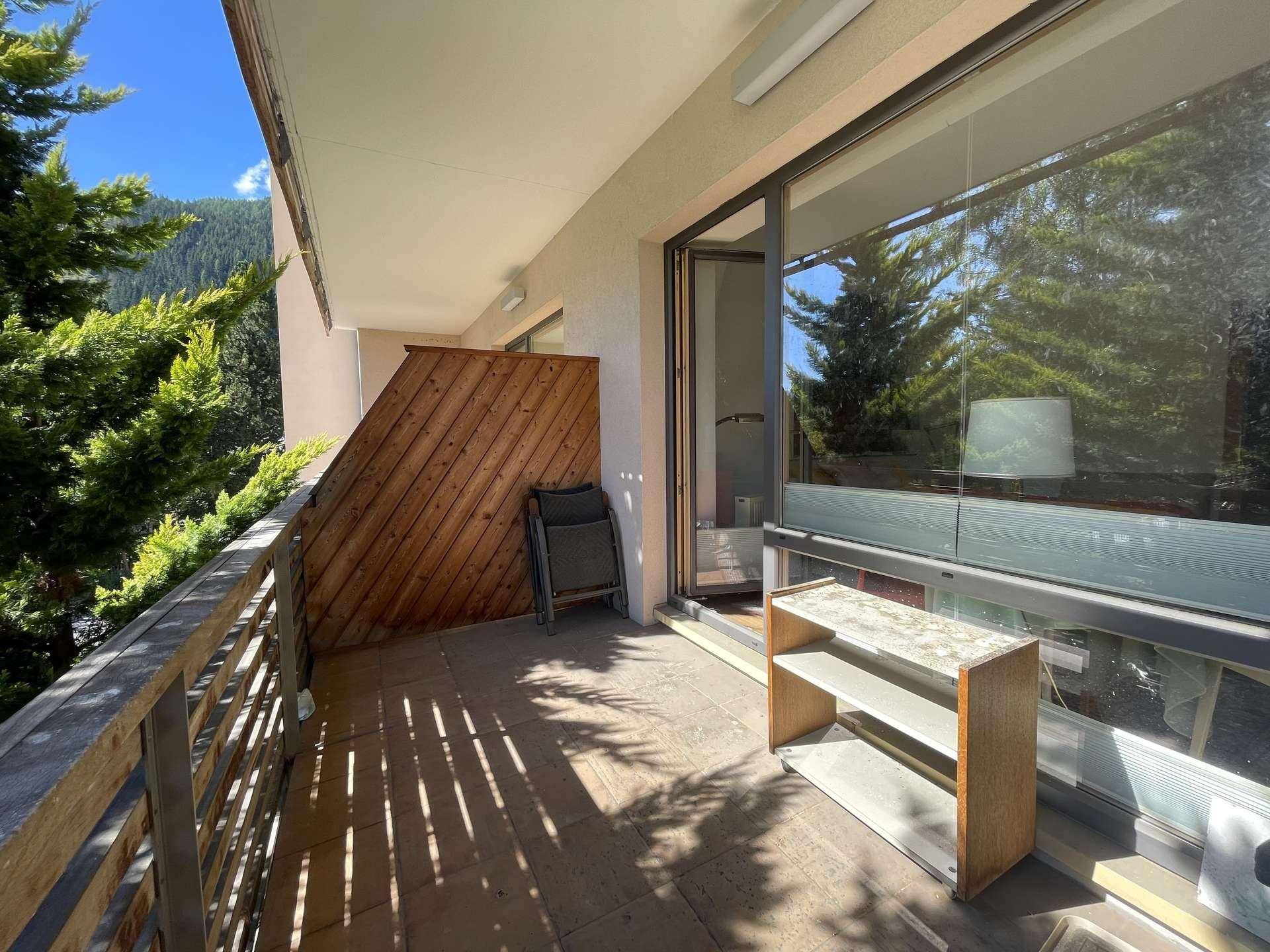 Sonniger Balkon mit Holzsichtschutz, Sitzgelegenheit und Blick auf die umliegende Natur.