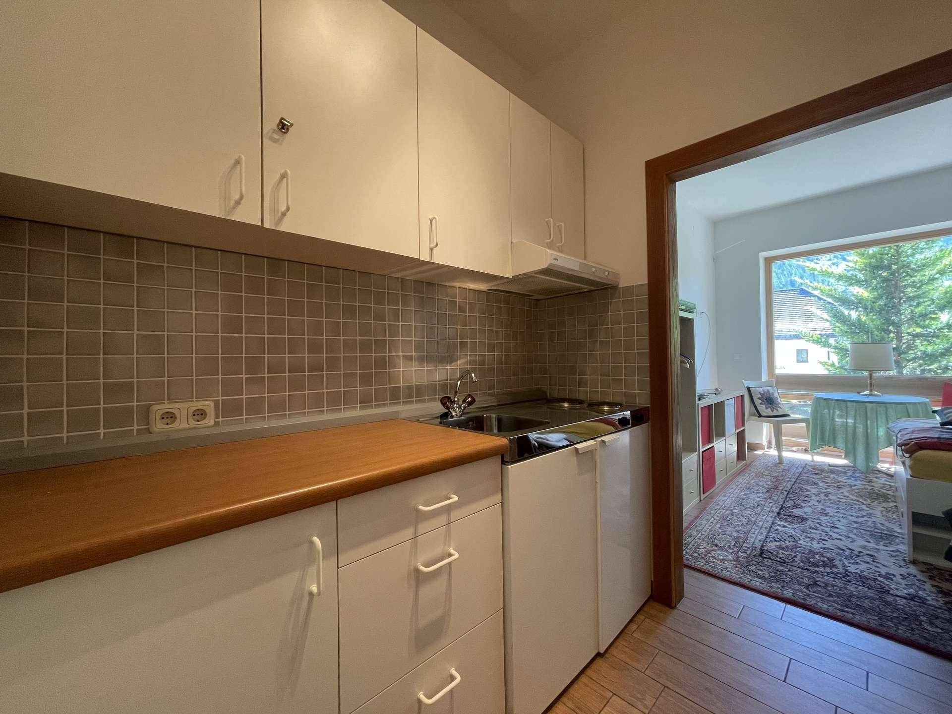 Funktionale Küchenzeile mit weißen Schränken, Holz-Arbeitsplatte und Blick in den Wohnbereich.