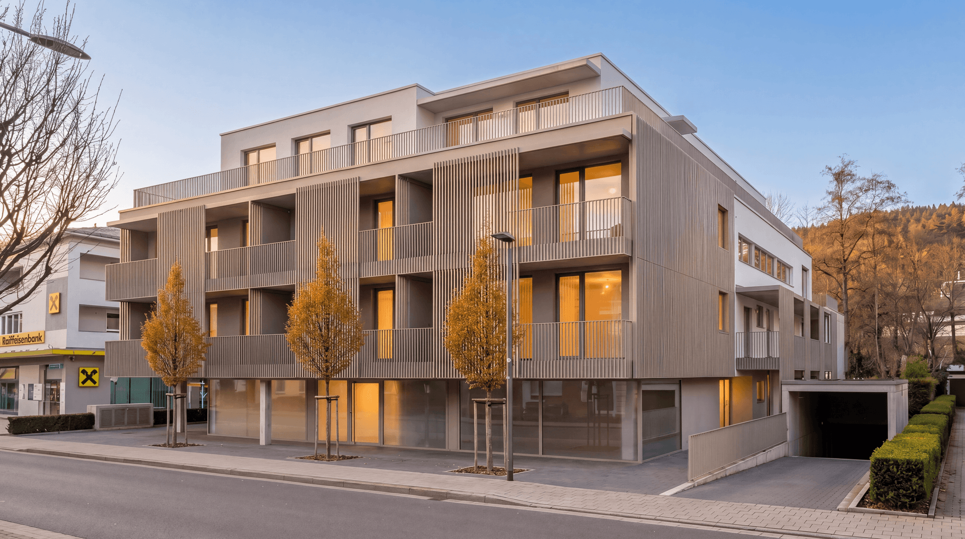 Ansicht des modernen Wohngebäudes von der Straßenseite mit Herbstbäumen und Tiefgaragenzufahrt.