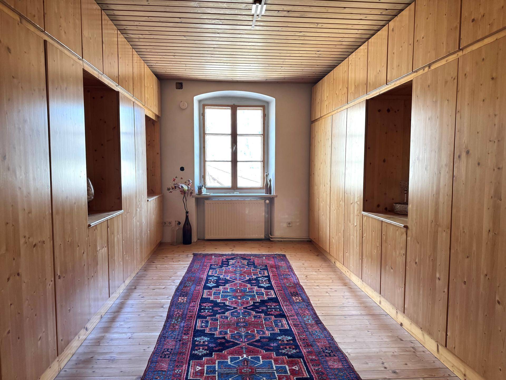 Flur mit eingebauten Holzschränken, Holzdielenboden und einem Fenster.