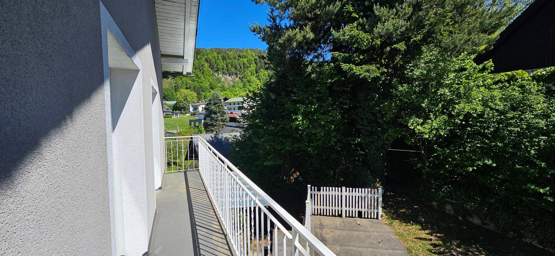 Schmaler Balkon mit weißem Geländer und Blick auf grüne Bäume und die umliegende Landschaft.