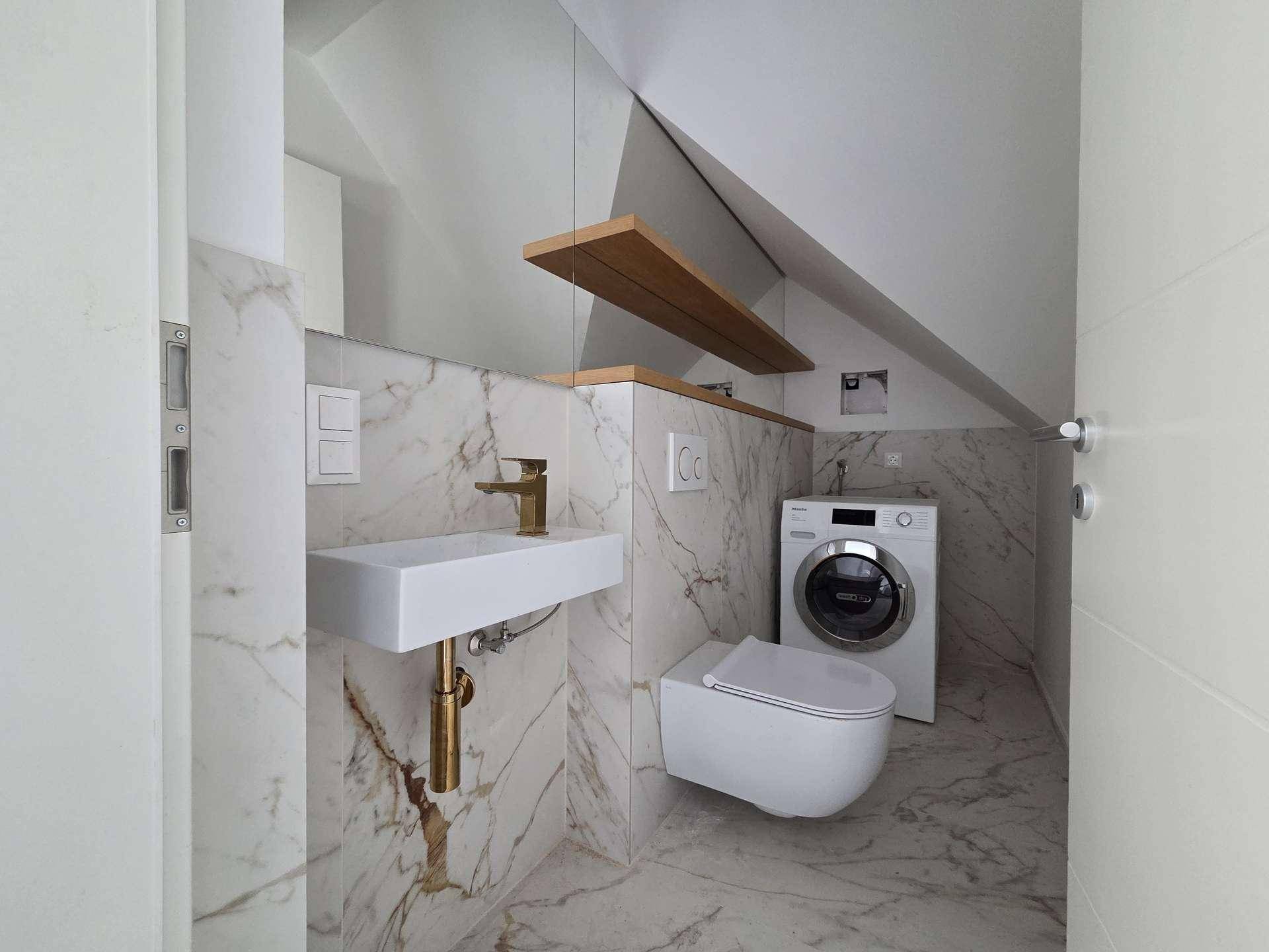 Kleines Badezimmer mit wandhängendem WC, Waschbecken, Waschmaschine und Marmorfliesen im Dachgeschoss.