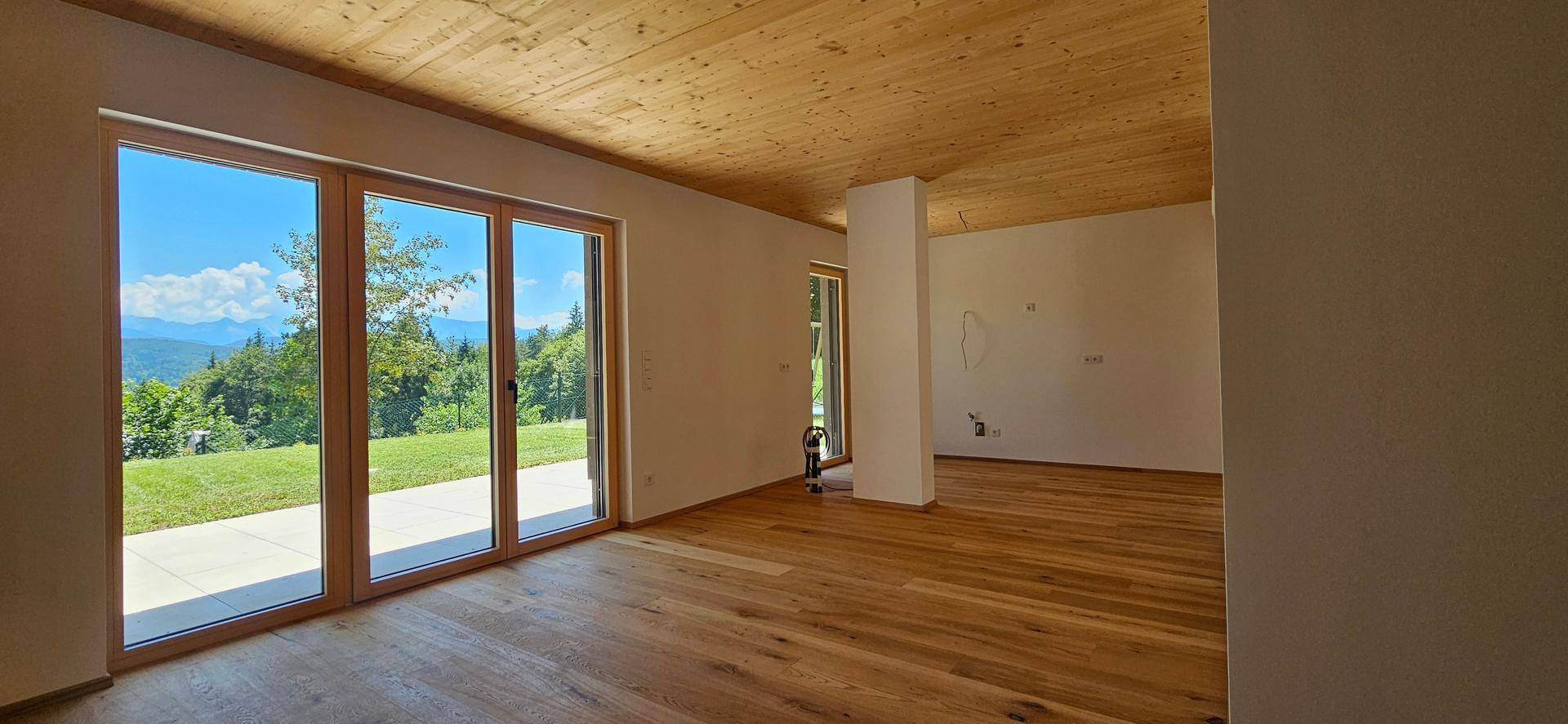 Lichtdurchfluteter Raum mit Holzboden, Holzdecke und großen Fenstern, die einen Panoramablick bieten.