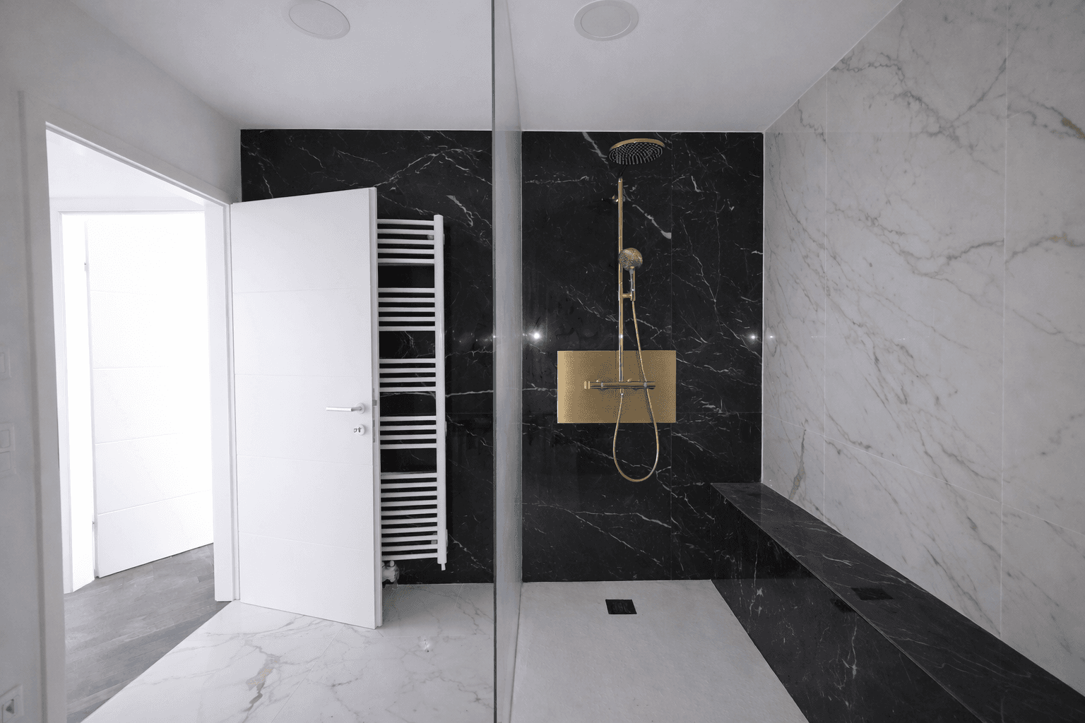 Modernes Badezimmer mit schwarzen und weißen Marmorfliesen, begehbarer Dusche und goldener Regendusche.