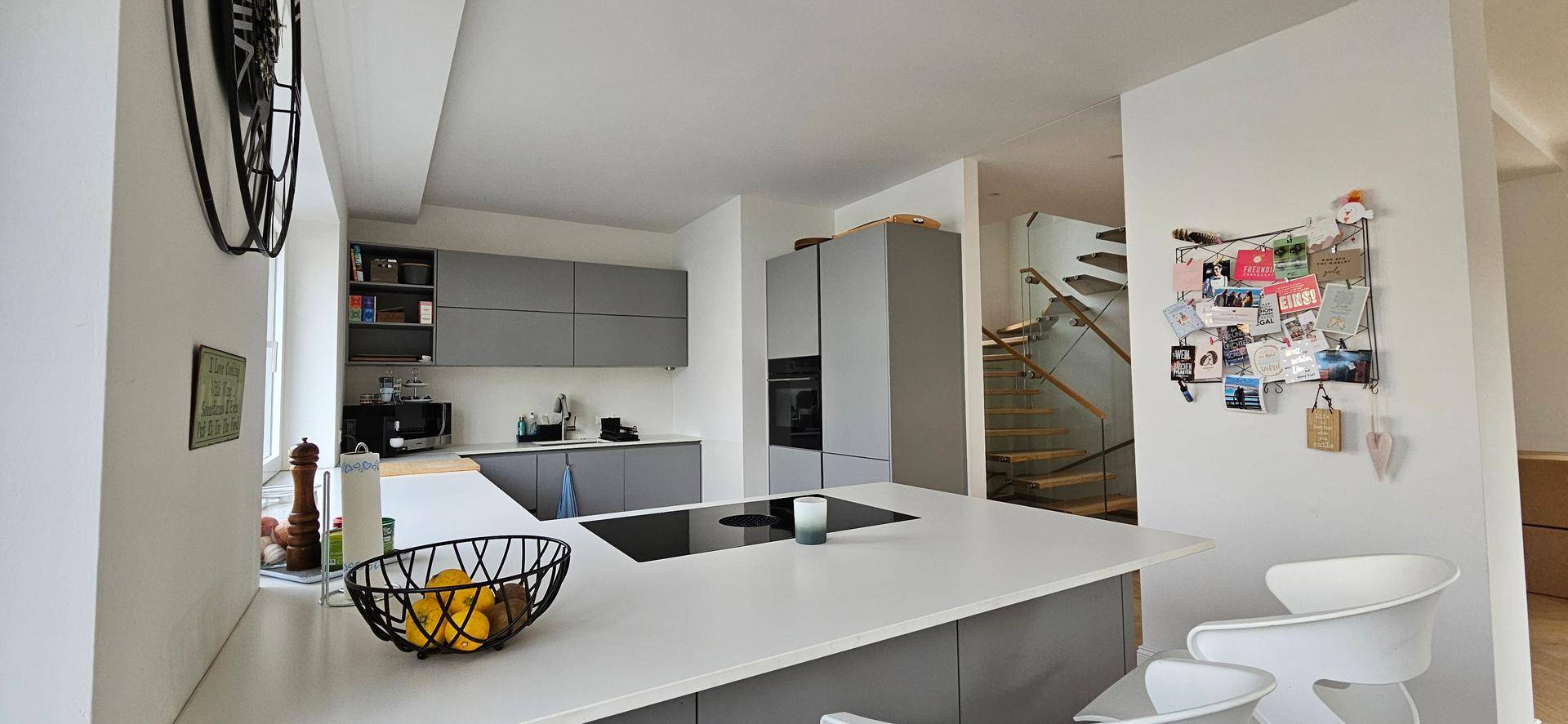 Moderne offene Küche mit grauen Schränken, Kochinsel und Blick auf die Treppe.