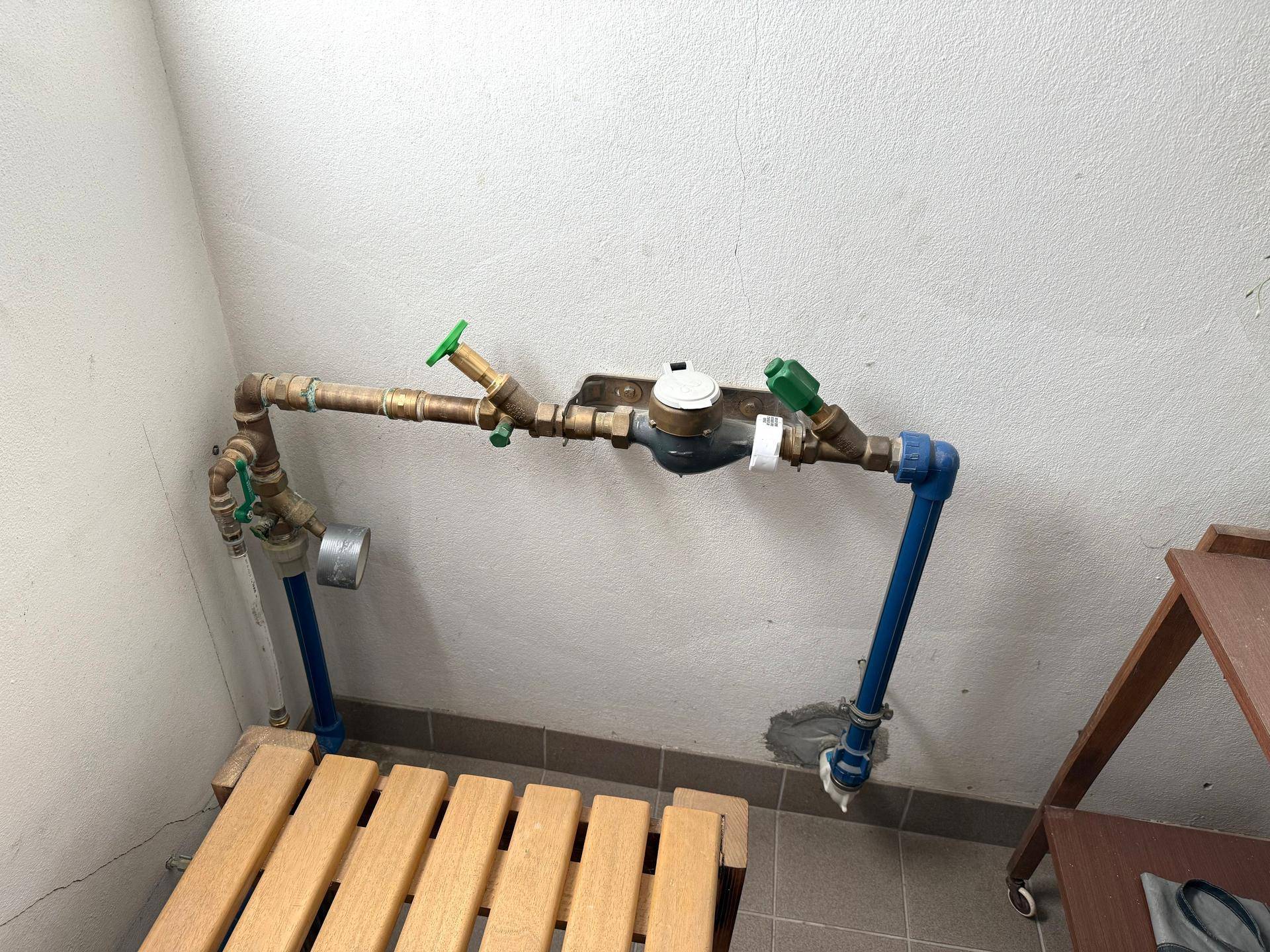 Installationsbereich mit Wasserzähler und Rohrleitungen, ordentlich auf einer Holzbank montiert.