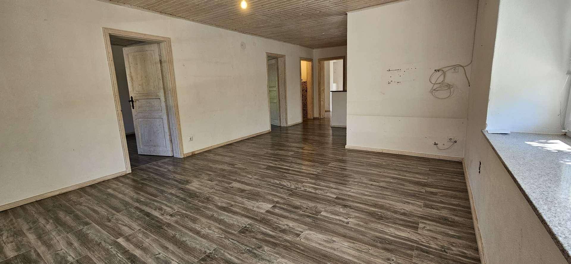 Heller Wohnraum mit Holzdielen-Decke und Laminatboden, der in einen Flur führt.