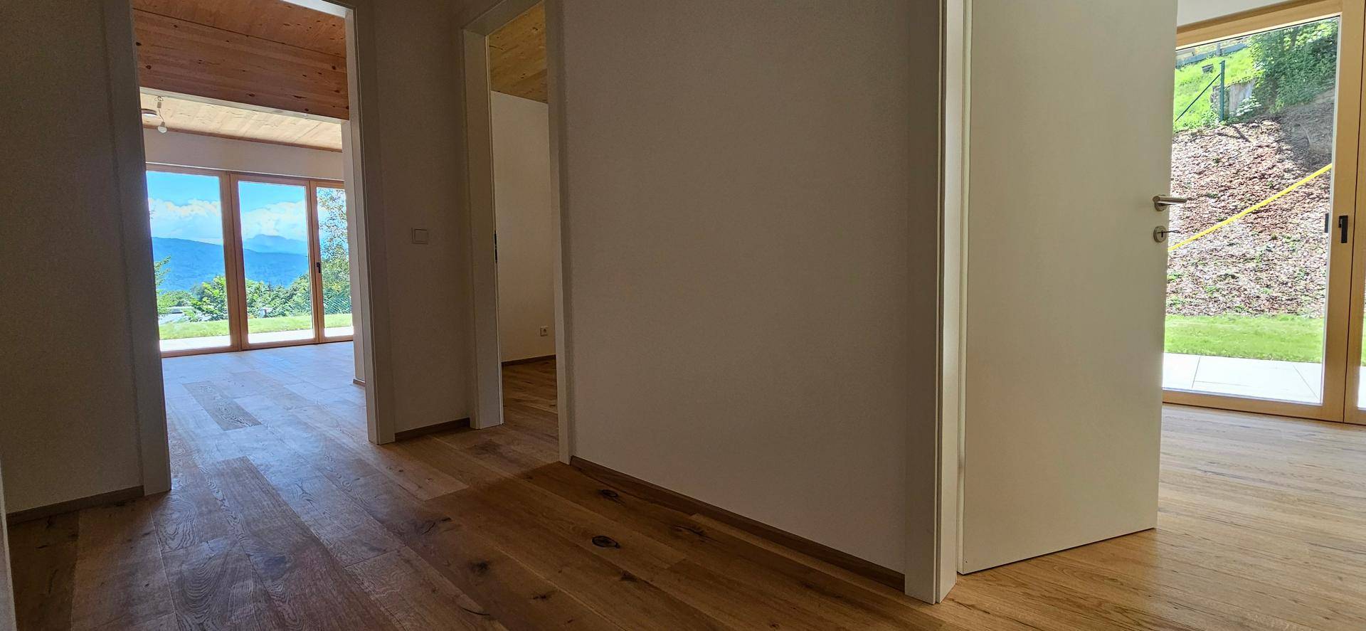 Heller Flur mit Holzboden und Zugang zu weiteren Räumen mit großen Fenstern und Bergblick.