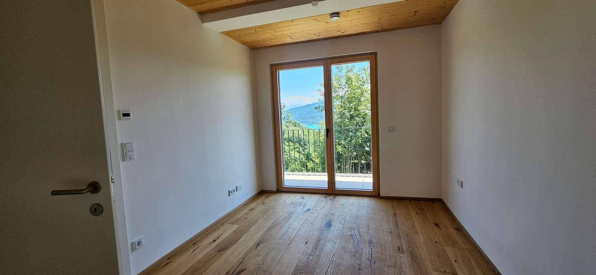 Schlafzimmer mit Holzboden, Holzdecke und Zugang zu einem Balkon mit malerischem Seeblick.
