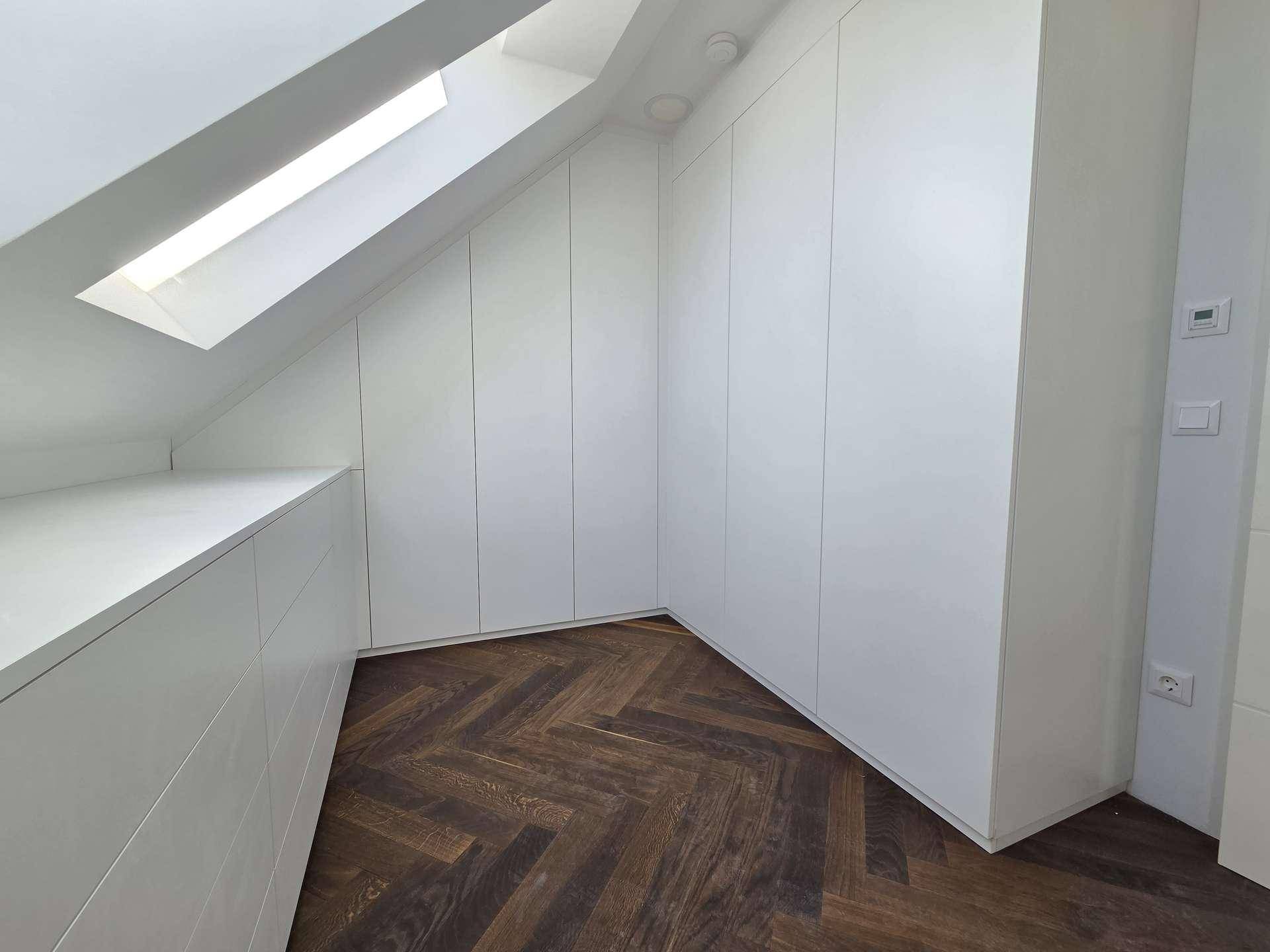 Dachgeschosszimmer mit maßgefertigten weißen Einbauschränken, Dachschräge und Oberlicht.