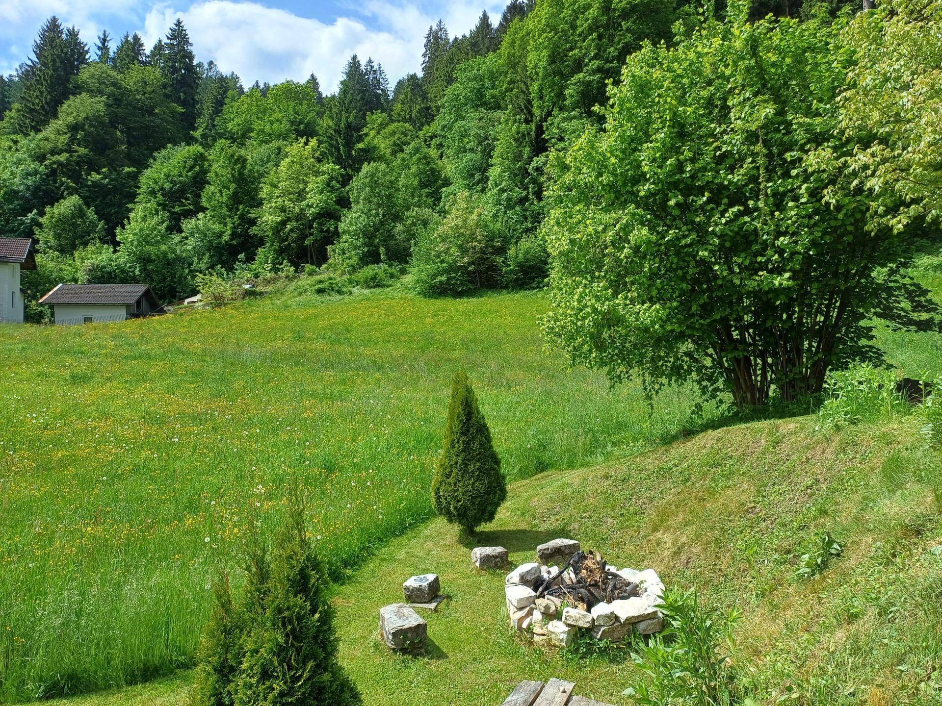 Grüne Gartenfläche mit Feuerstelle und Blick auf die umliegende Natur.