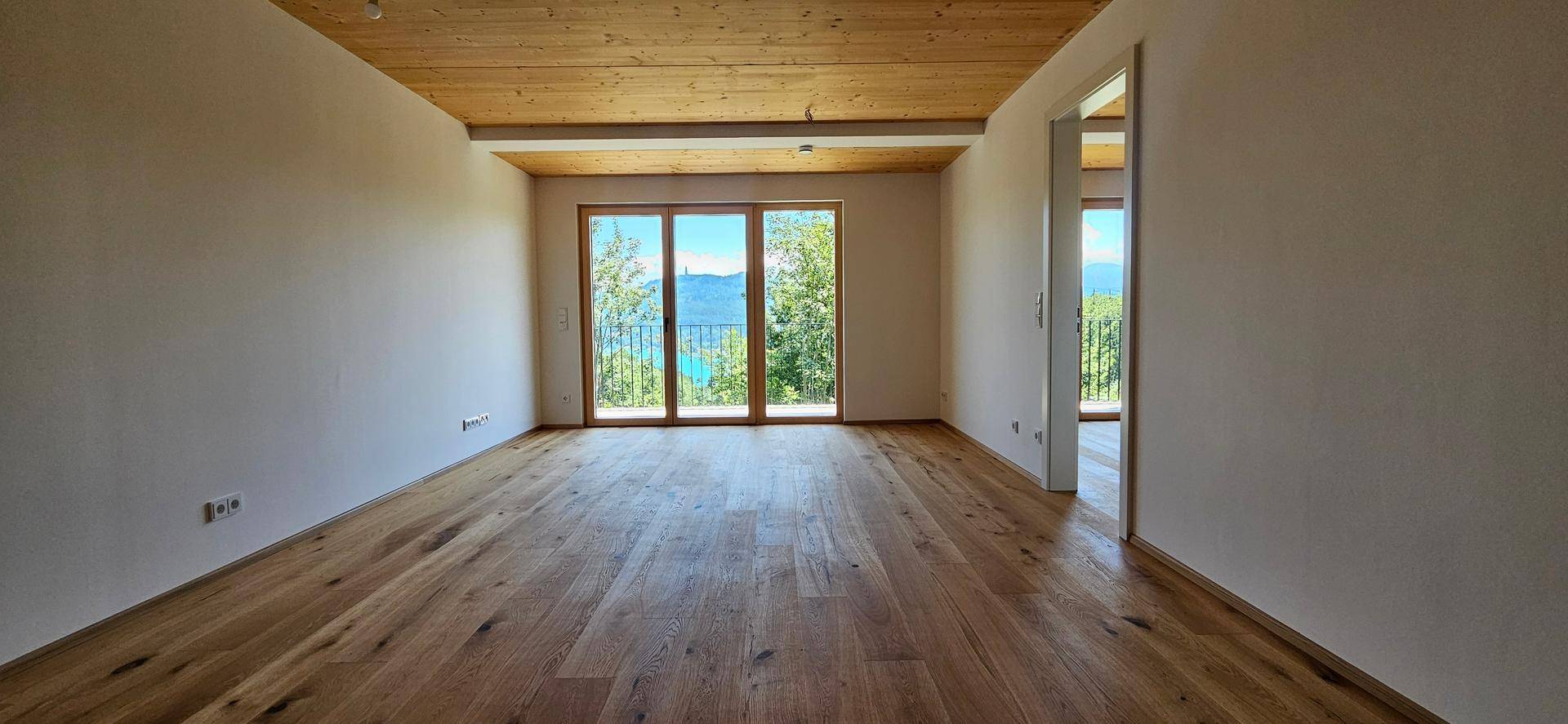 Heller Wohnraum mit Holzboden, Holzdecke und großen Fenstern mit Seeblick.