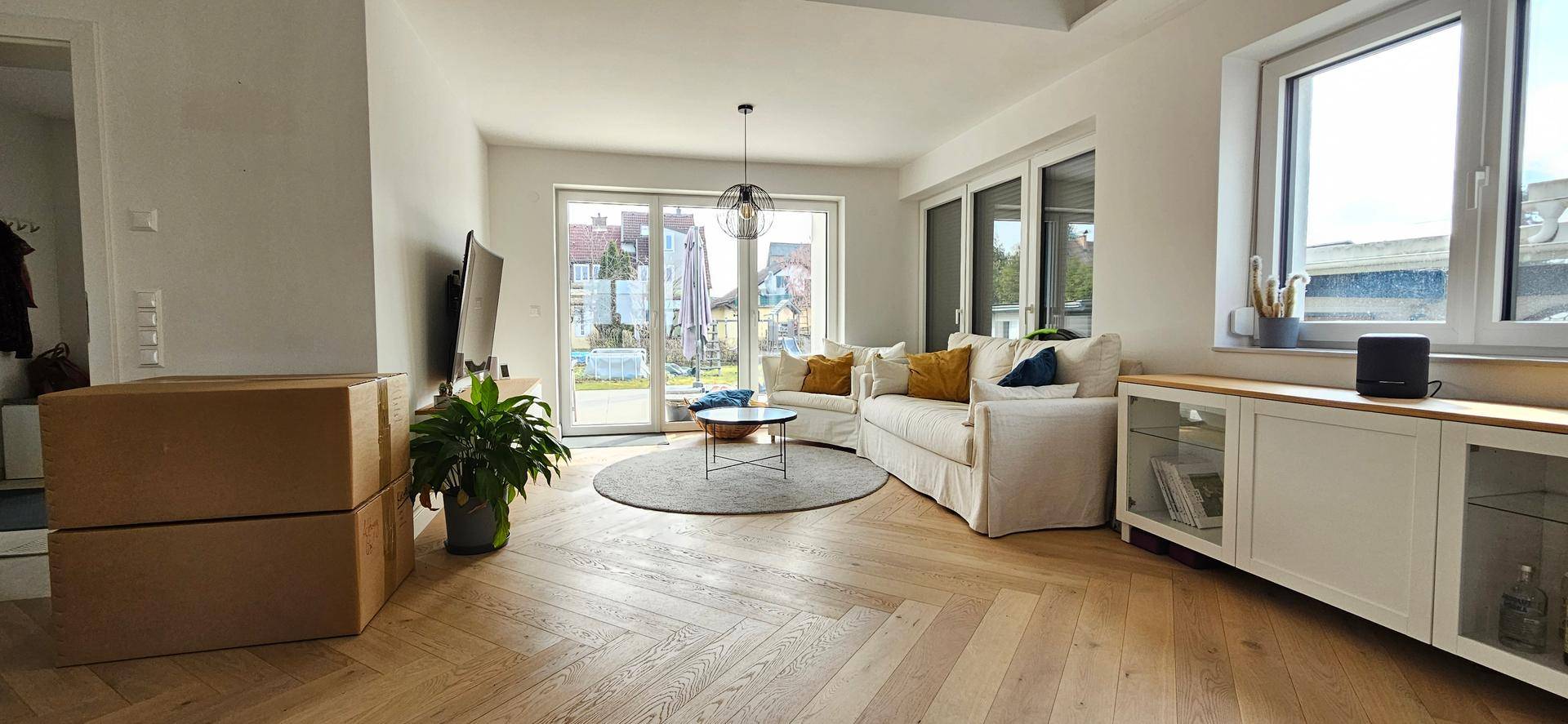 Geräumiges Wohnzimmer mit hellem Parkettboden, großen Fenstern und direktem Zugang zum Garten.