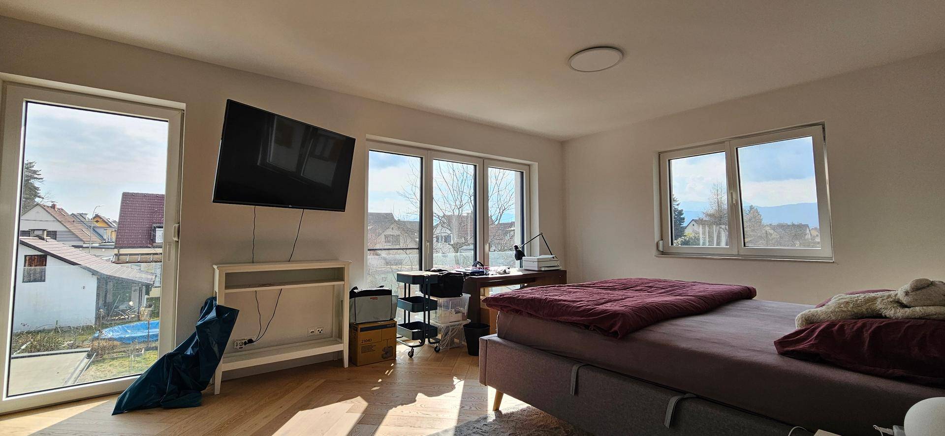 Helles Schlafzimmer mit großen Fenstern, Holzboden und Ausblick ins Grüne.