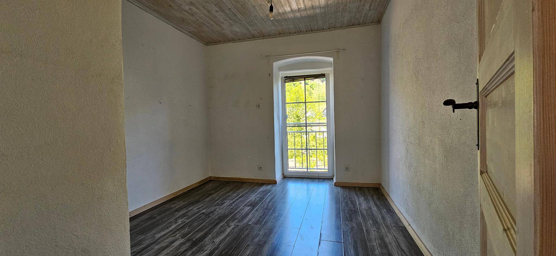 Helles Schlafzimmer mit Holzboden und einem hohen Fenster, das viel Licht hereinlässt.