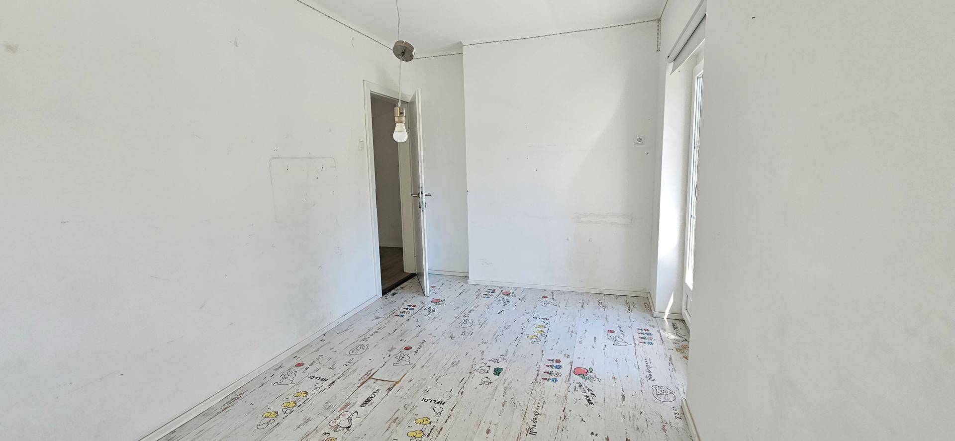 Einfaches Schlafzimmer mit hellem Boden und Türzugang zu einem weiteren Raum.