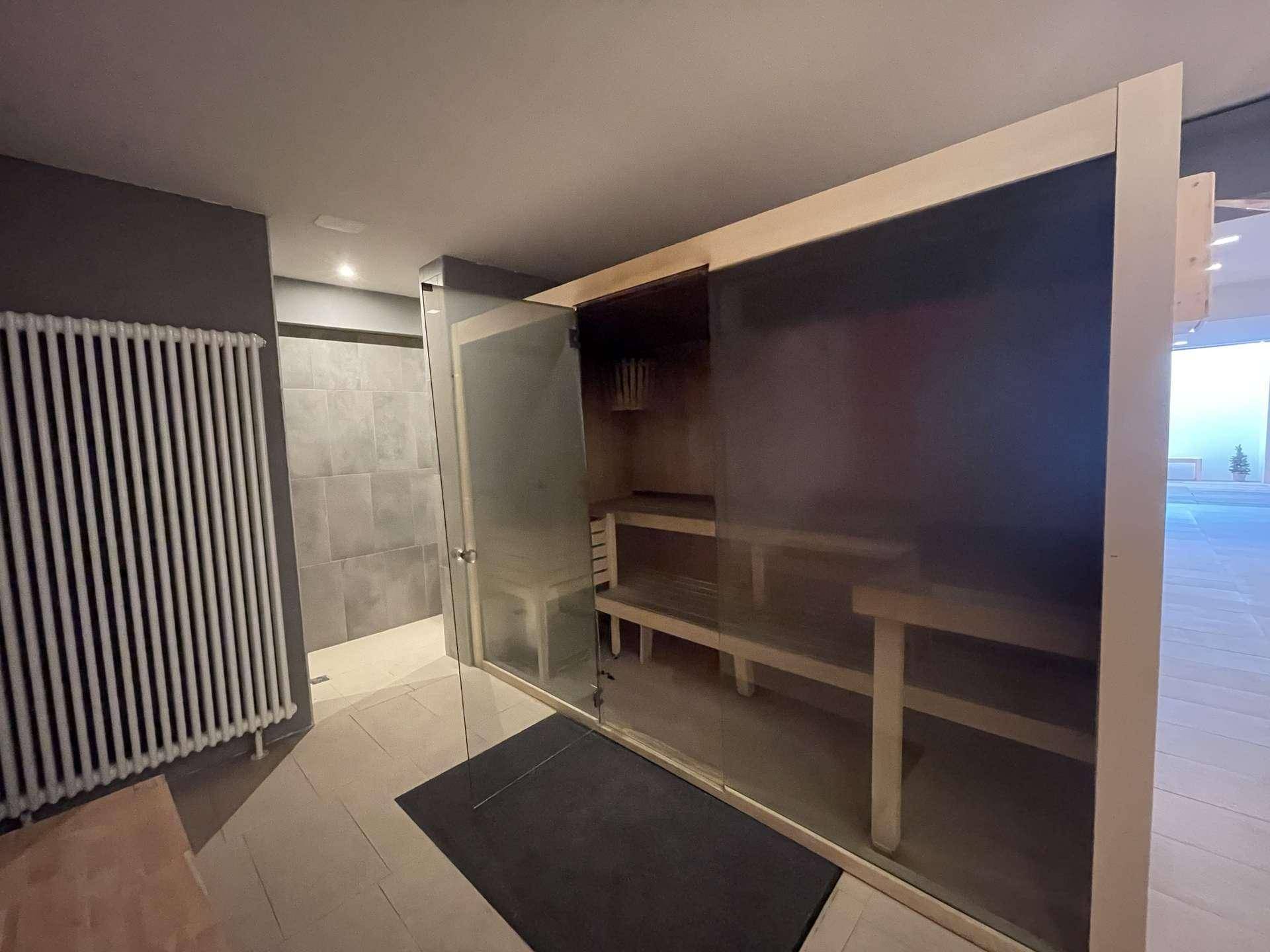Moderne Sauna mit Holzbänken und Glasfront, Teil eines umfassenden Wellnessbereichs.