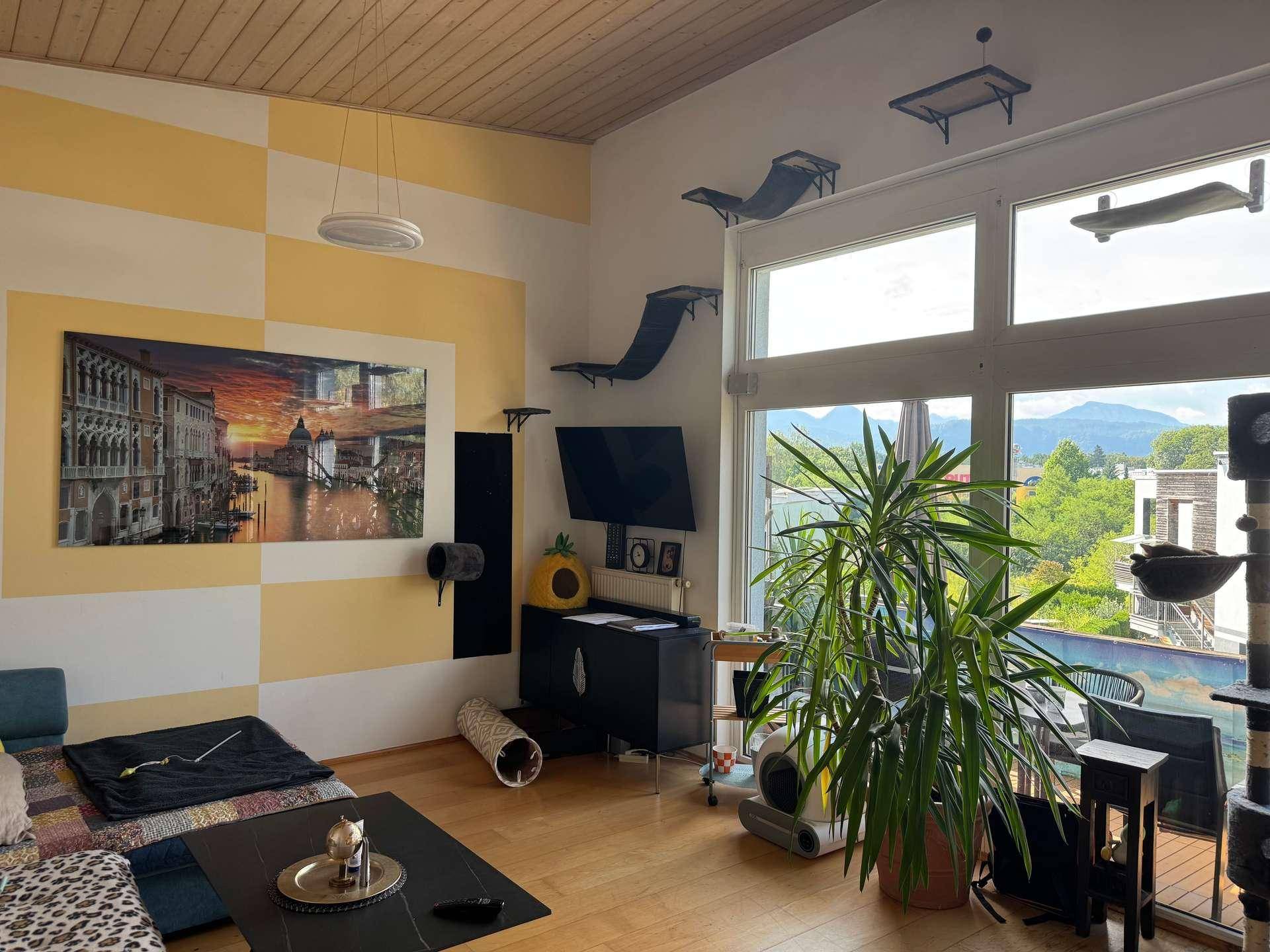 Helles Wohnzimmer mit großen Fenstern, Holzbalkendecke und Blick ins Grüne.