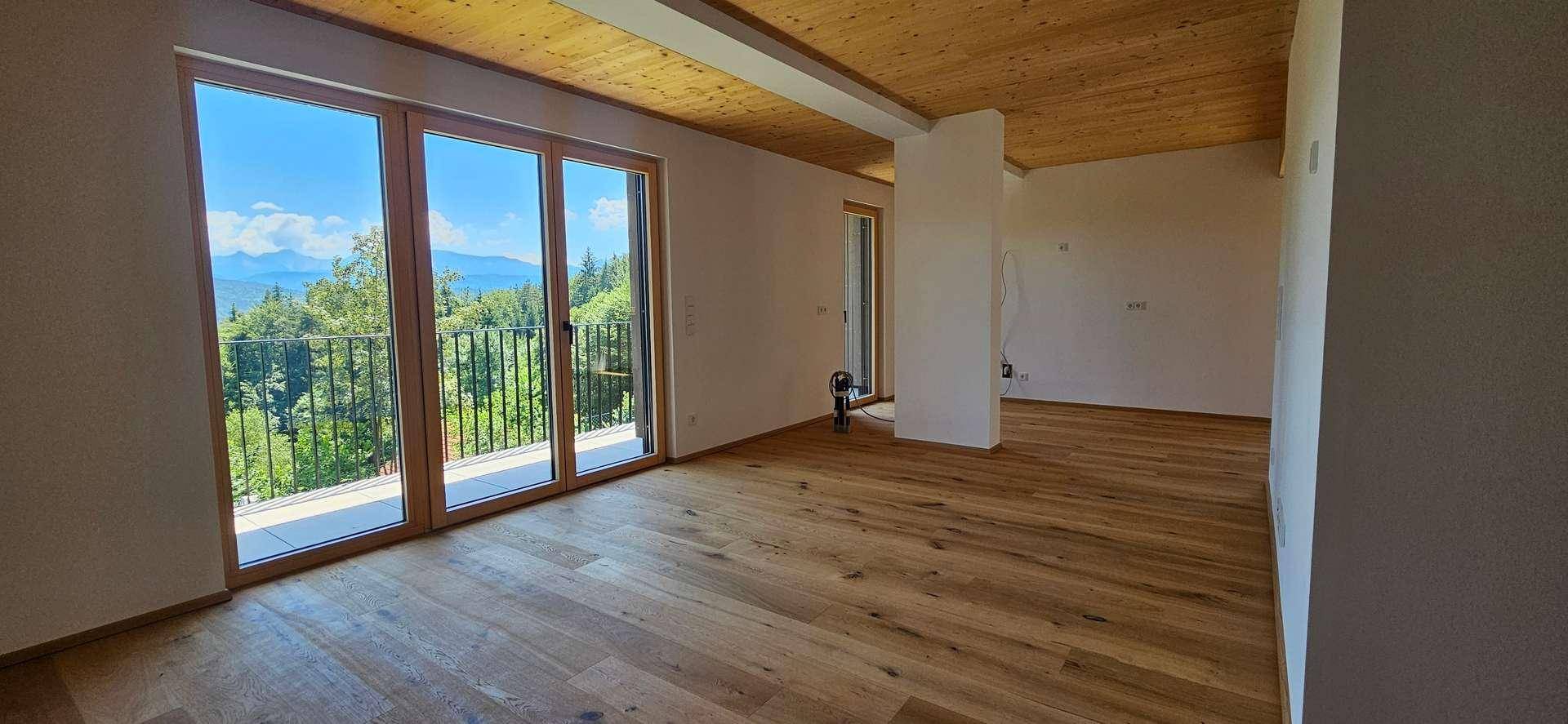 Geräumiger, heller Wohnbereich mit Holzboden, Holzdecke und Zugang zu einem Balkon mit grüner Aussicht.