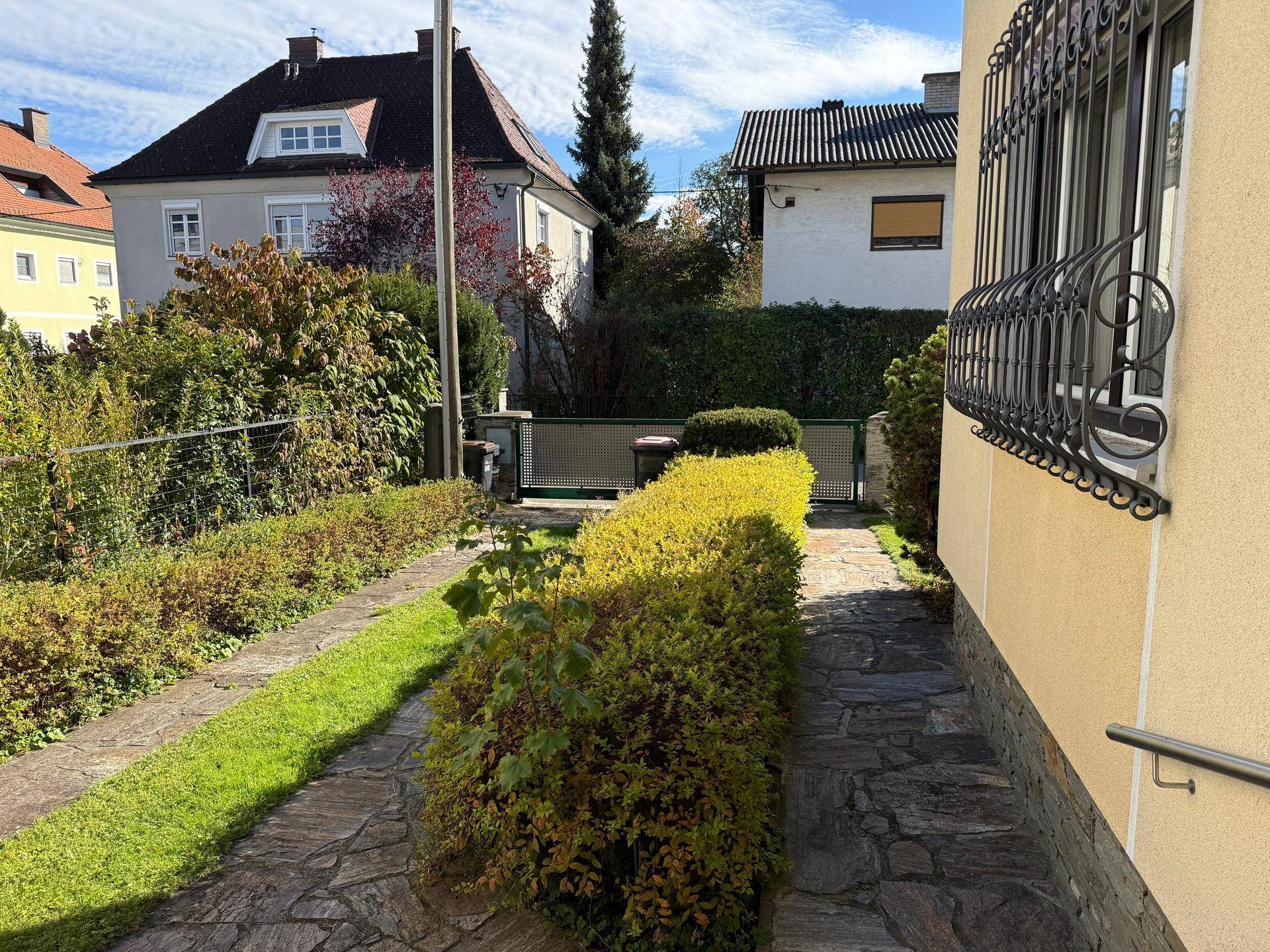 Seitenweg entlang des Hauses mit gepflegter Hecke und Zugang zum Gartenbereich.