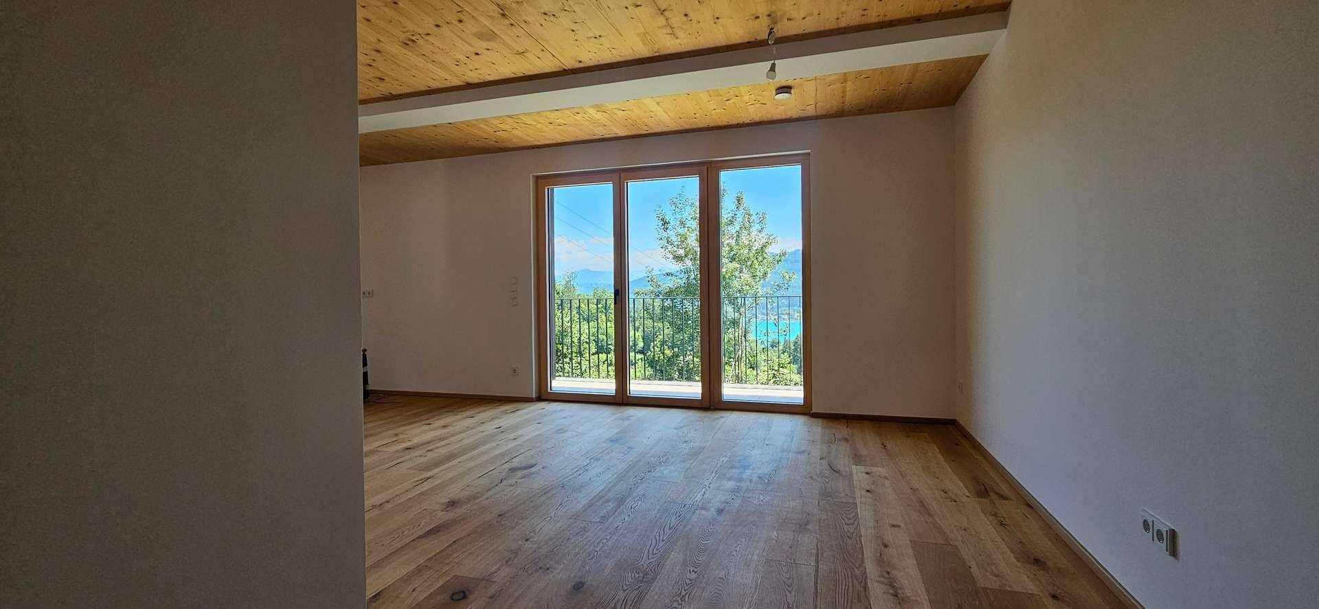 Lichtdurchfluteter Raum mit Holzboden und Holzdecke, große Fensterfront mit Seeblick.