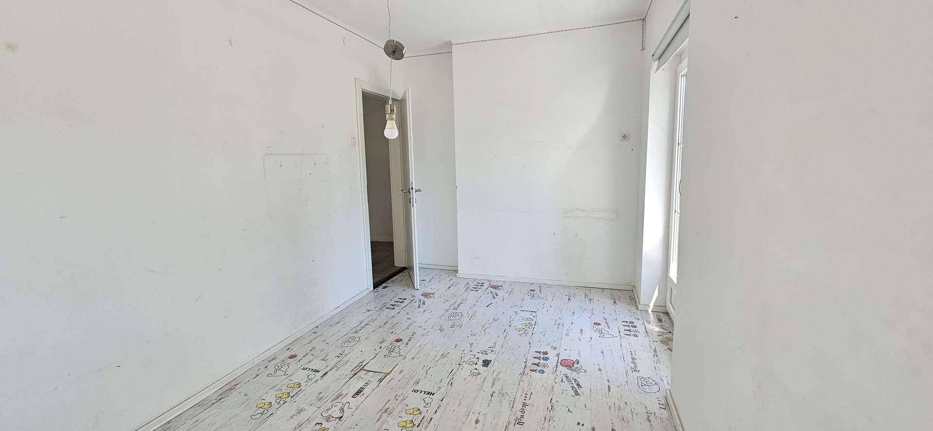 Einfaches Schlafzimmer mit gemustertem Boden und weißen Wänden, bereit zur individuellen Gestaltung.