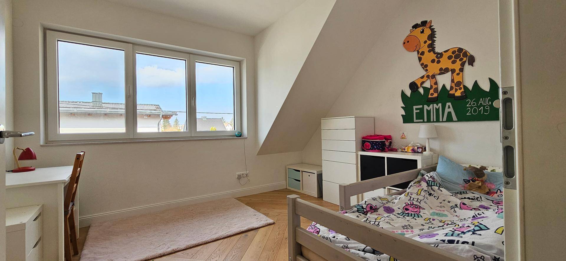 Kinderzimmer mit Dachschräge, hellem Holzboden und großem Fenster für viel Tageslicht.