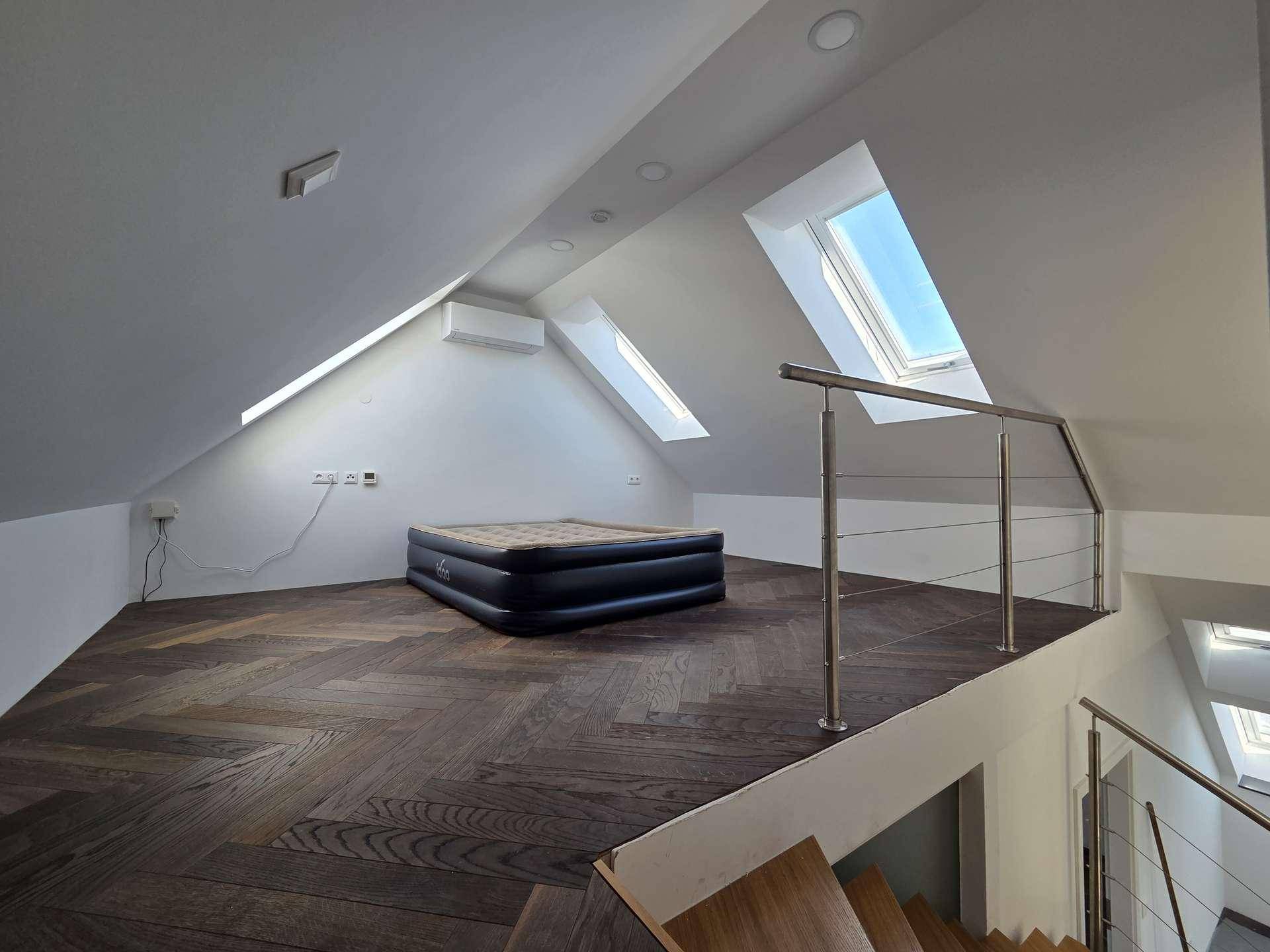 Helle Galerie im Dachgeschoss mit Dachschrägen, Oberlichtern und dunklem Fischgrätparkett.